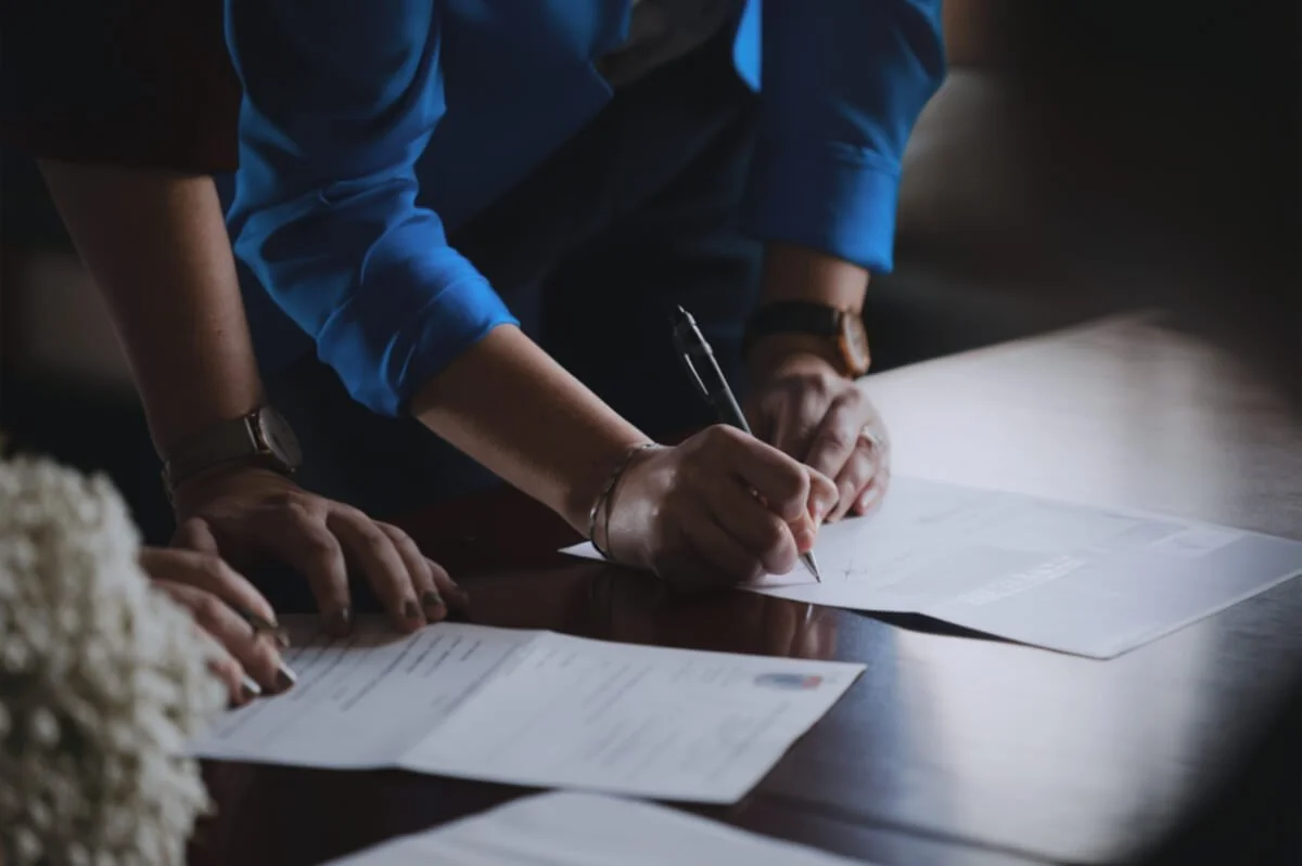Zwei Personen unterschreiben Dokumente auf einem Tisch – Symbol für die zuverlässige Erledigung aller Formalitäten bei Veerman Bestattungen.