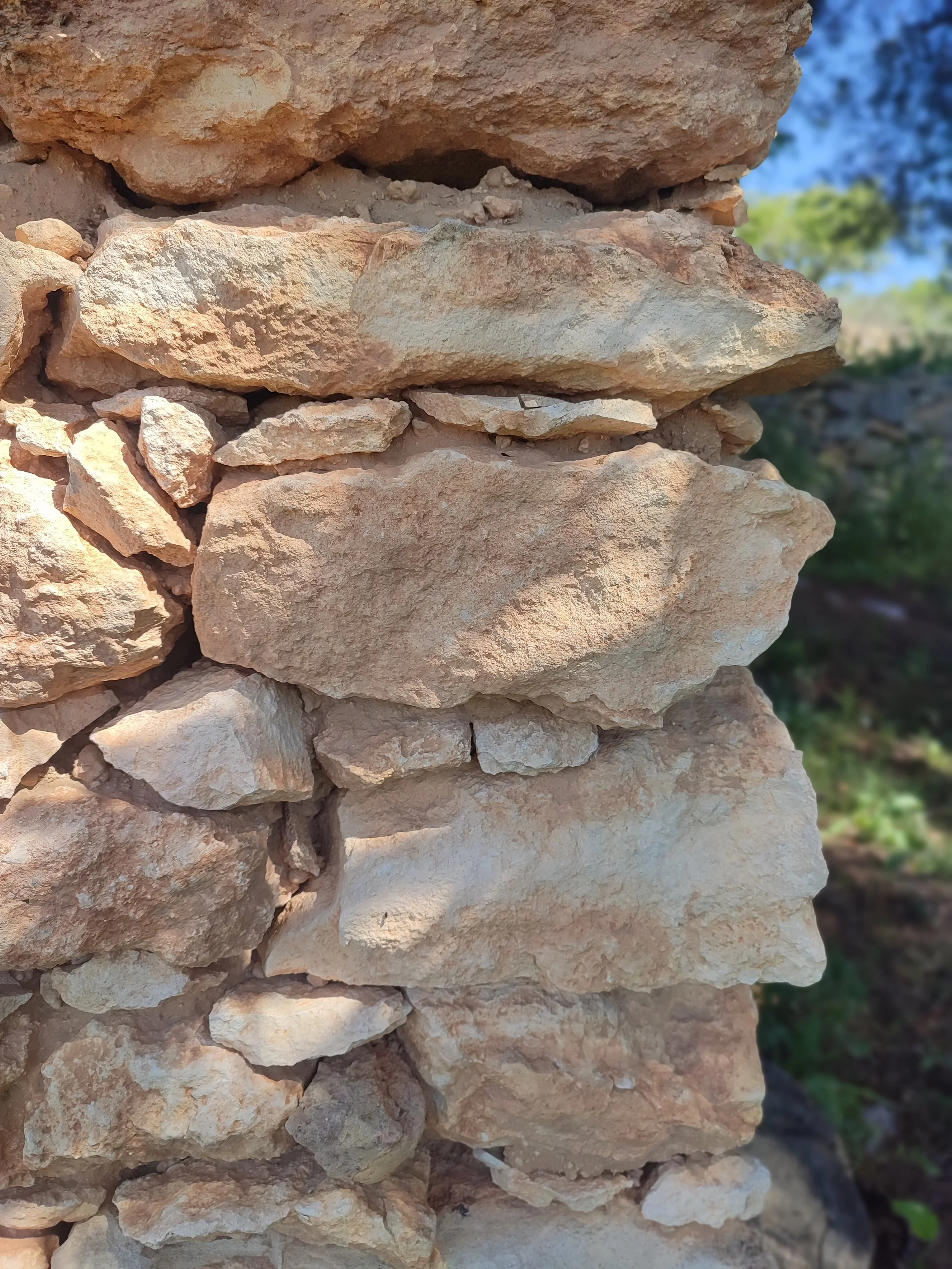 Close-up of a stacked stone wall with beige and light brown rocks, some gradation and texture visible.