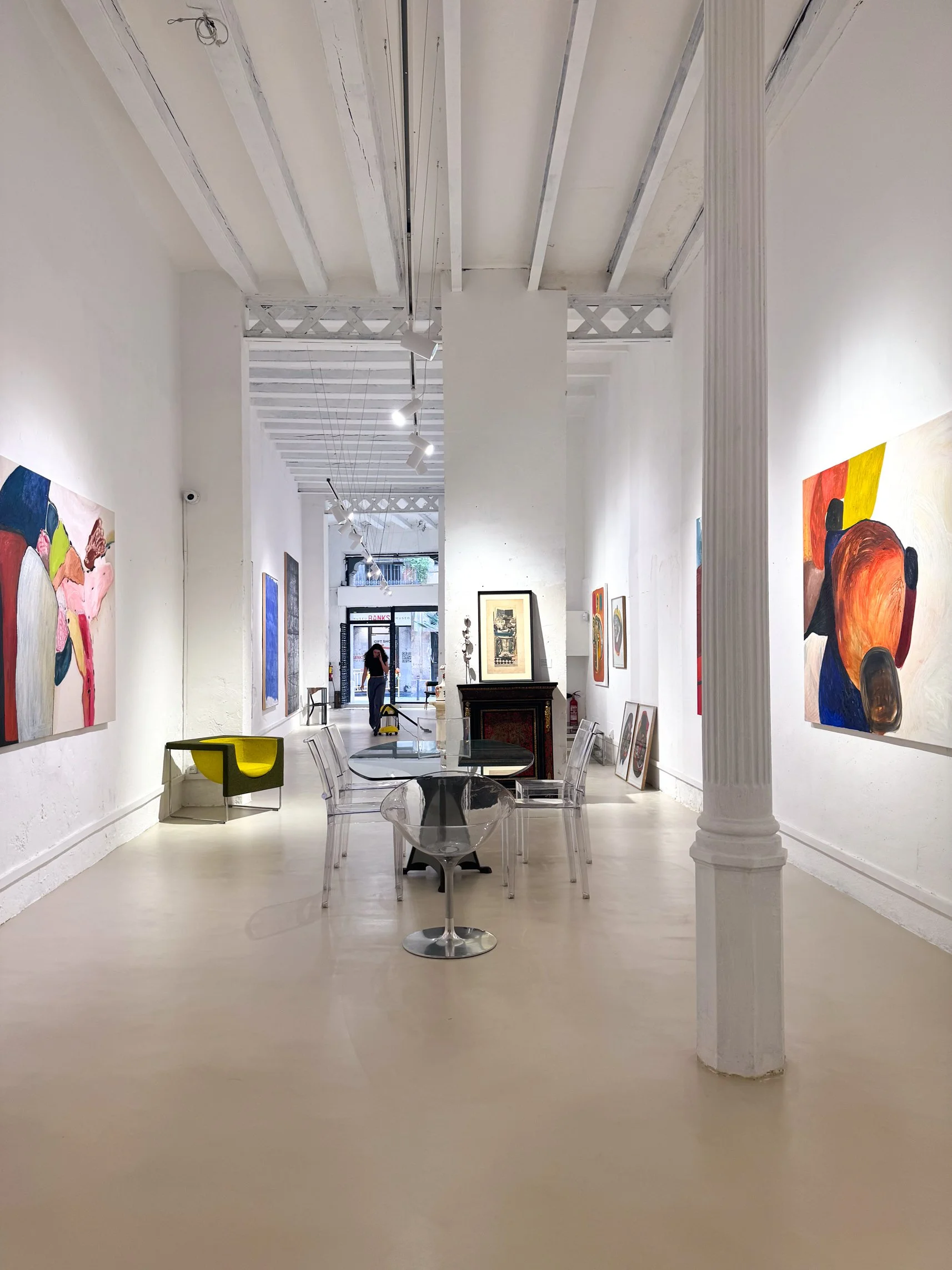 Espacio de alquiler de Matiz Gallery en Barcelona con pinturas de Nina Akhobadze, mesa Alada de Oscar Tusquets y sillas transparentes de Philippe Starck.