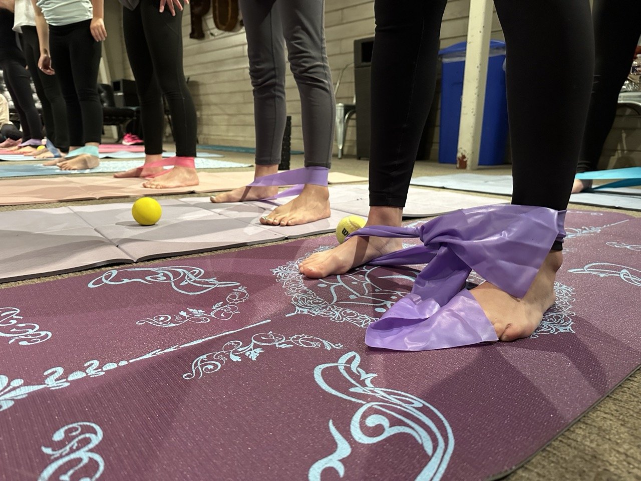 Close up of people standing on yoga mats with resistance bands around ankles