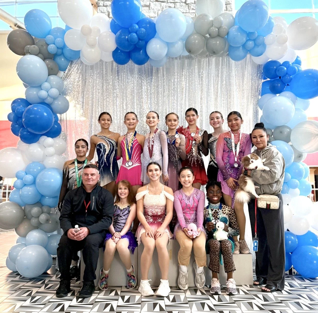 Team of figure skaters posing in competition dresses with coaches