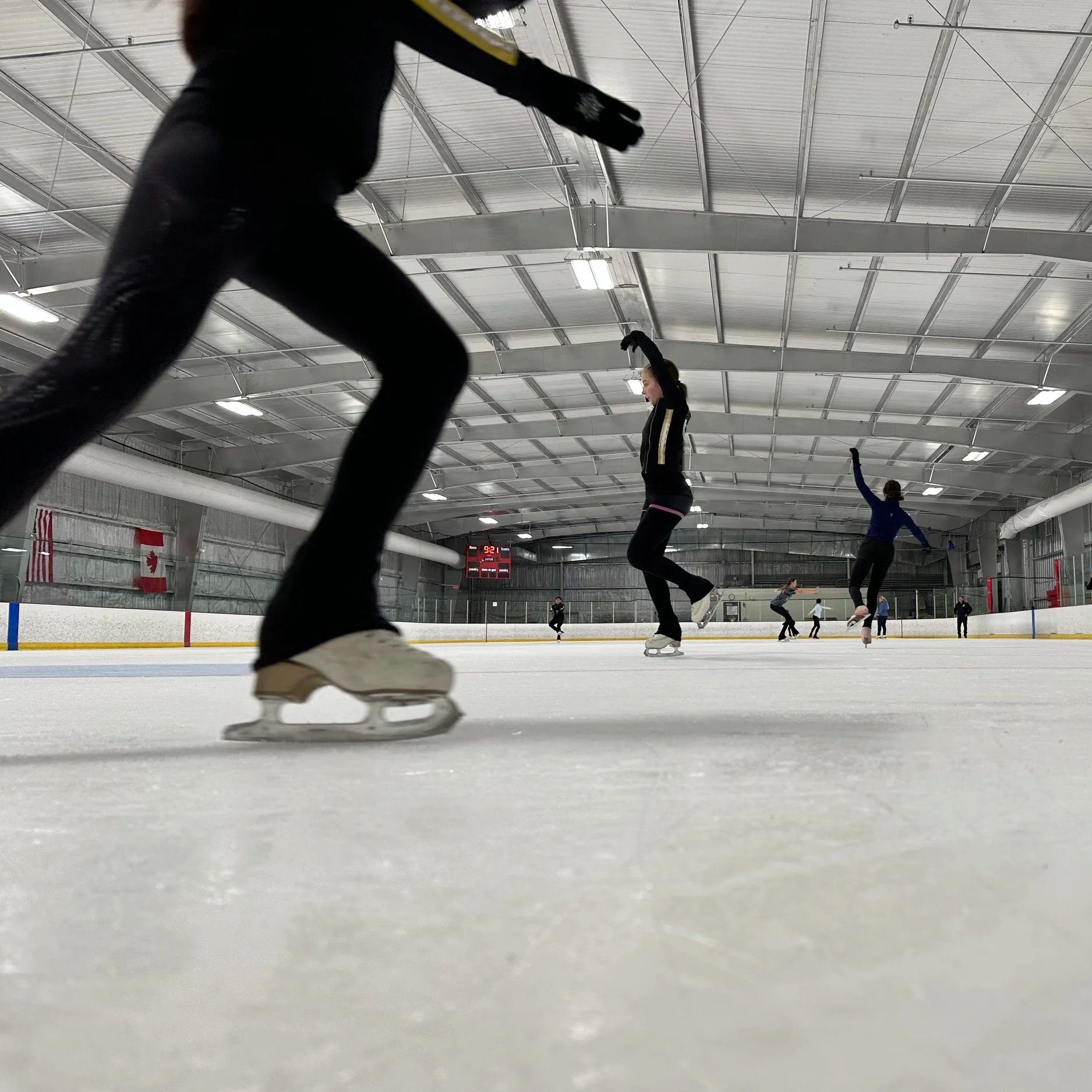 People ice skating at an indoor rink, seen from a low angle.