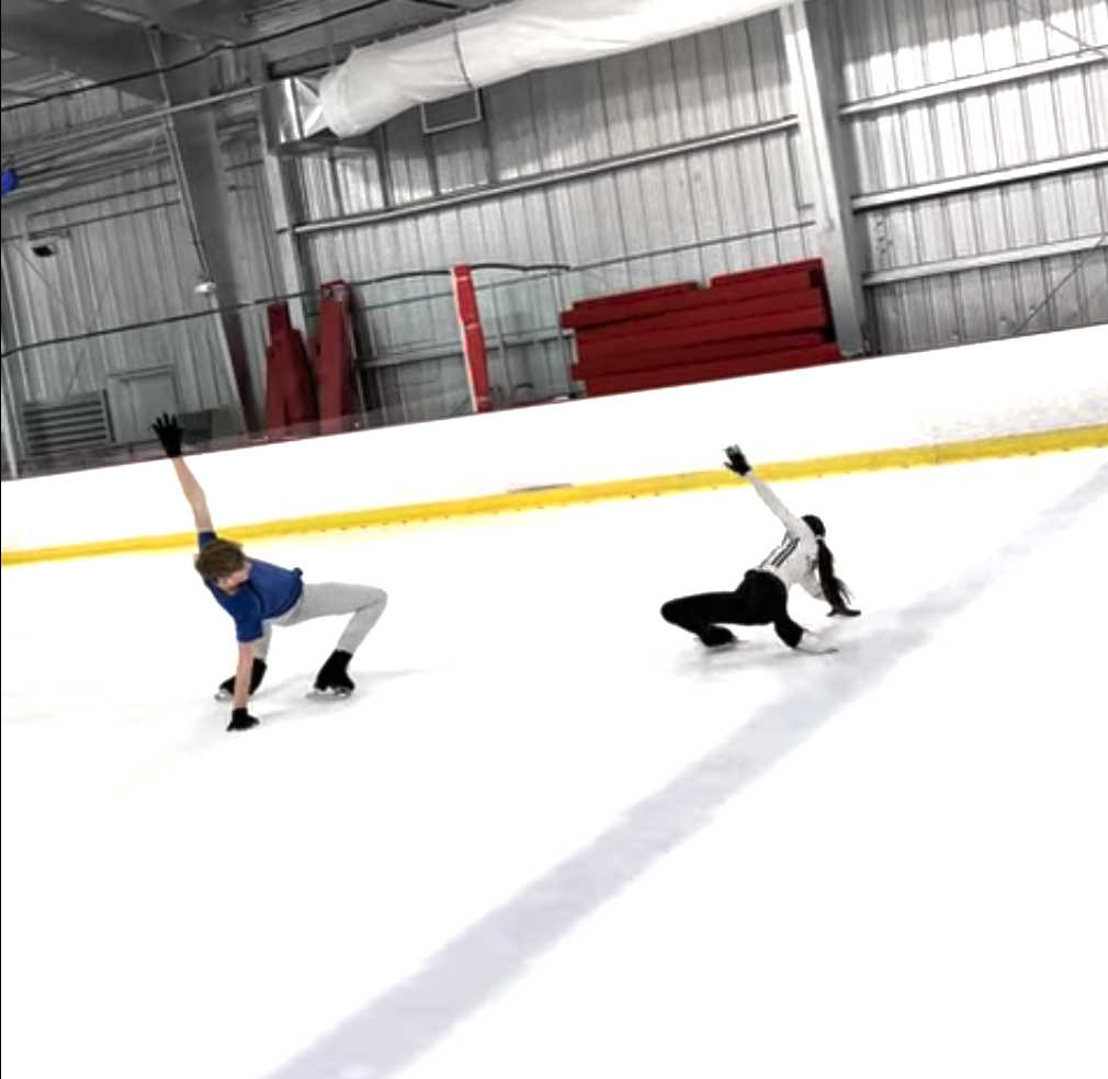 Two people practicing dance or gymnastics on an ice rink, one in a blue shirt and gray pants, the other in a white shirt and black pants, both in poses on the ice.