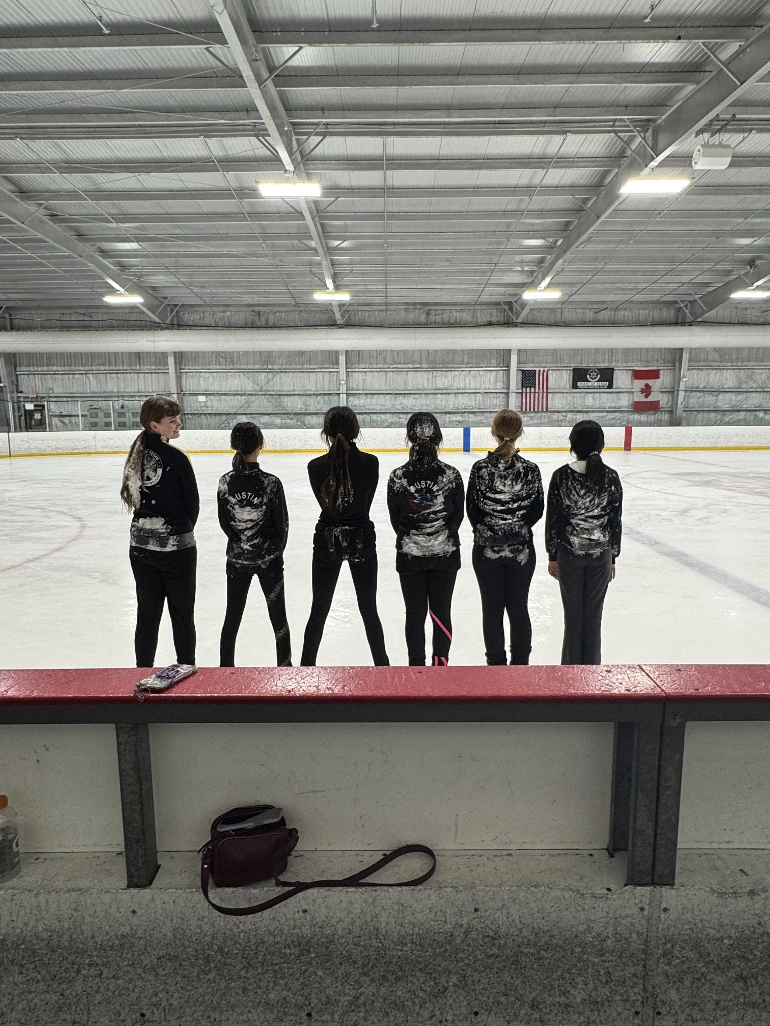 Figure skaters stand on the ice with their backs to the camera. covered in snow and ice
