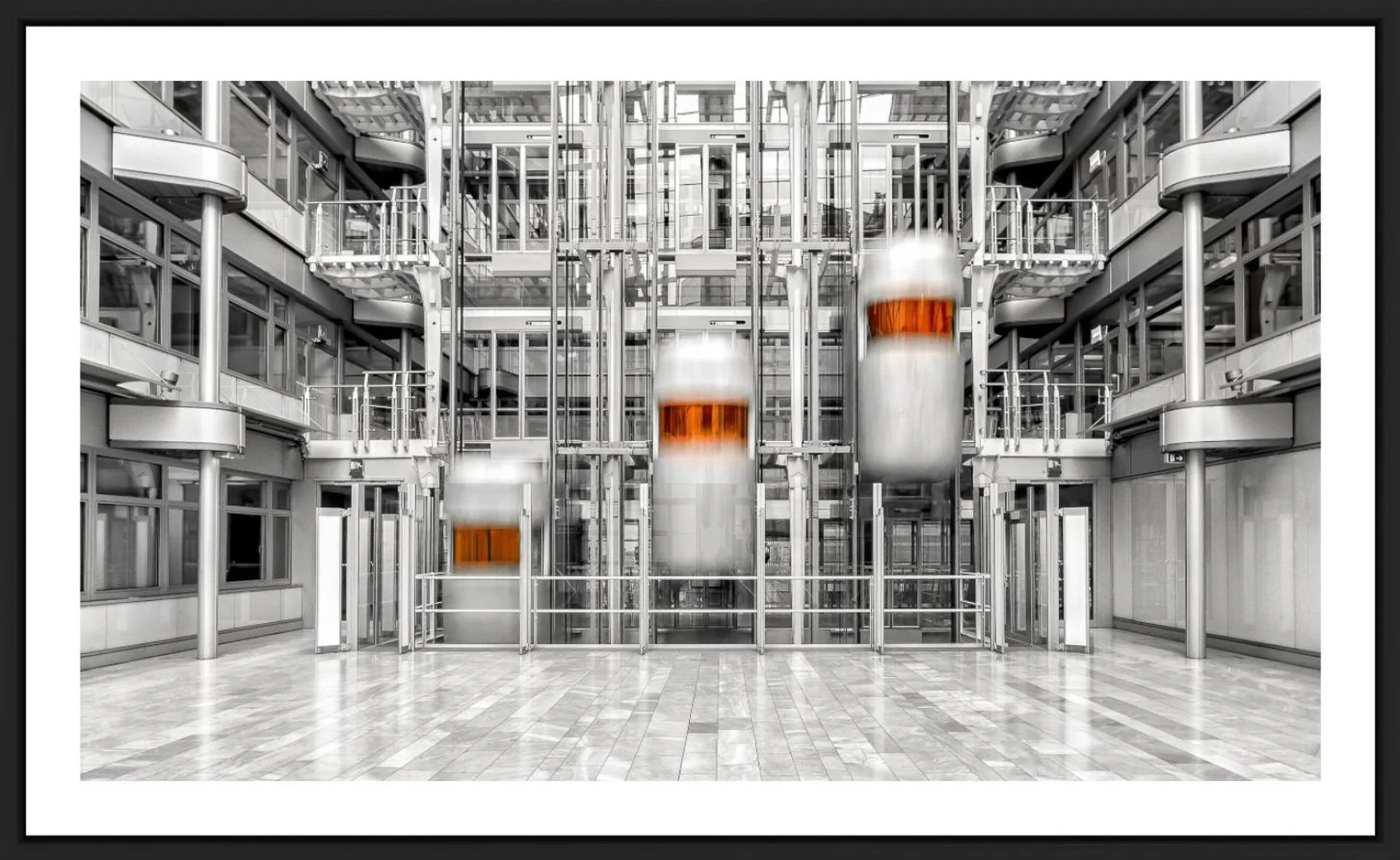 Moderne Aufzugsanlage mit vier Glastüren und Edelstahlrahmen in einem offenen Gebäudefoyer, teilweise in Schwarz-Weiß gehalten, mit einer Holzfußboden.