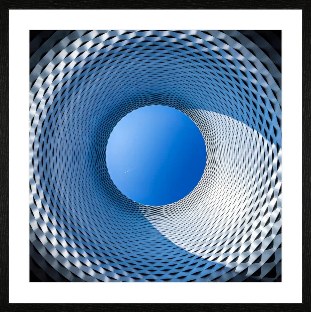 Ansicht eines zylindrischen Gebäudes mit einer spiralförmigen, gitterartigen Struktur, die nach oben zur blauen Himmelöffnung führt.