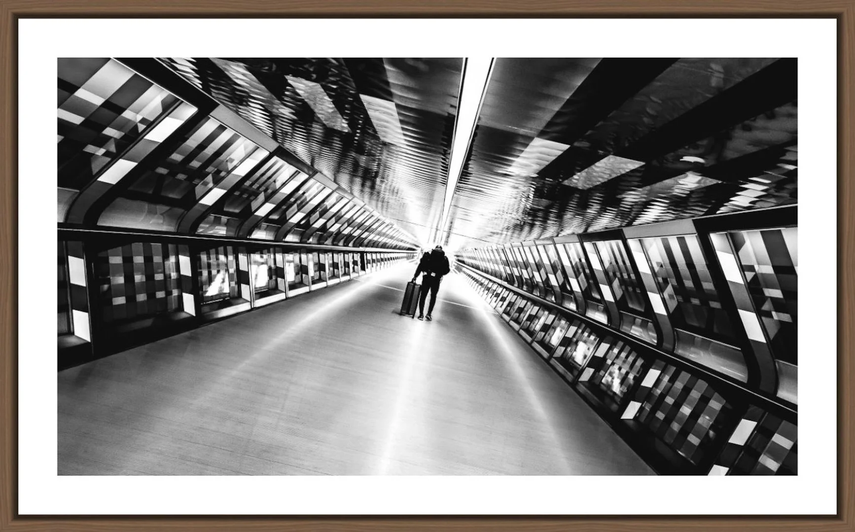 Ein Mann mit einem Reisekoffer läuft durch eine moderne, reflektierende Architektur, die an einem Flughafen oder Bahnhof sein könnte, in schwarz-weiß.