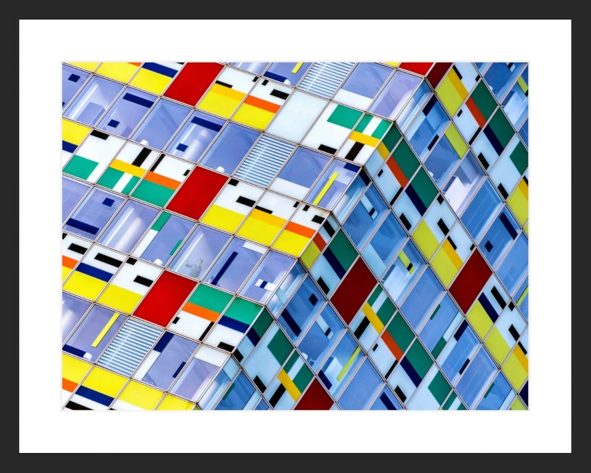 Blick auf die bunte Fassade eines modernen Gebäudes mit geometrischen Mustern aus bunt lackierten Fenstern und Metallrahmen.