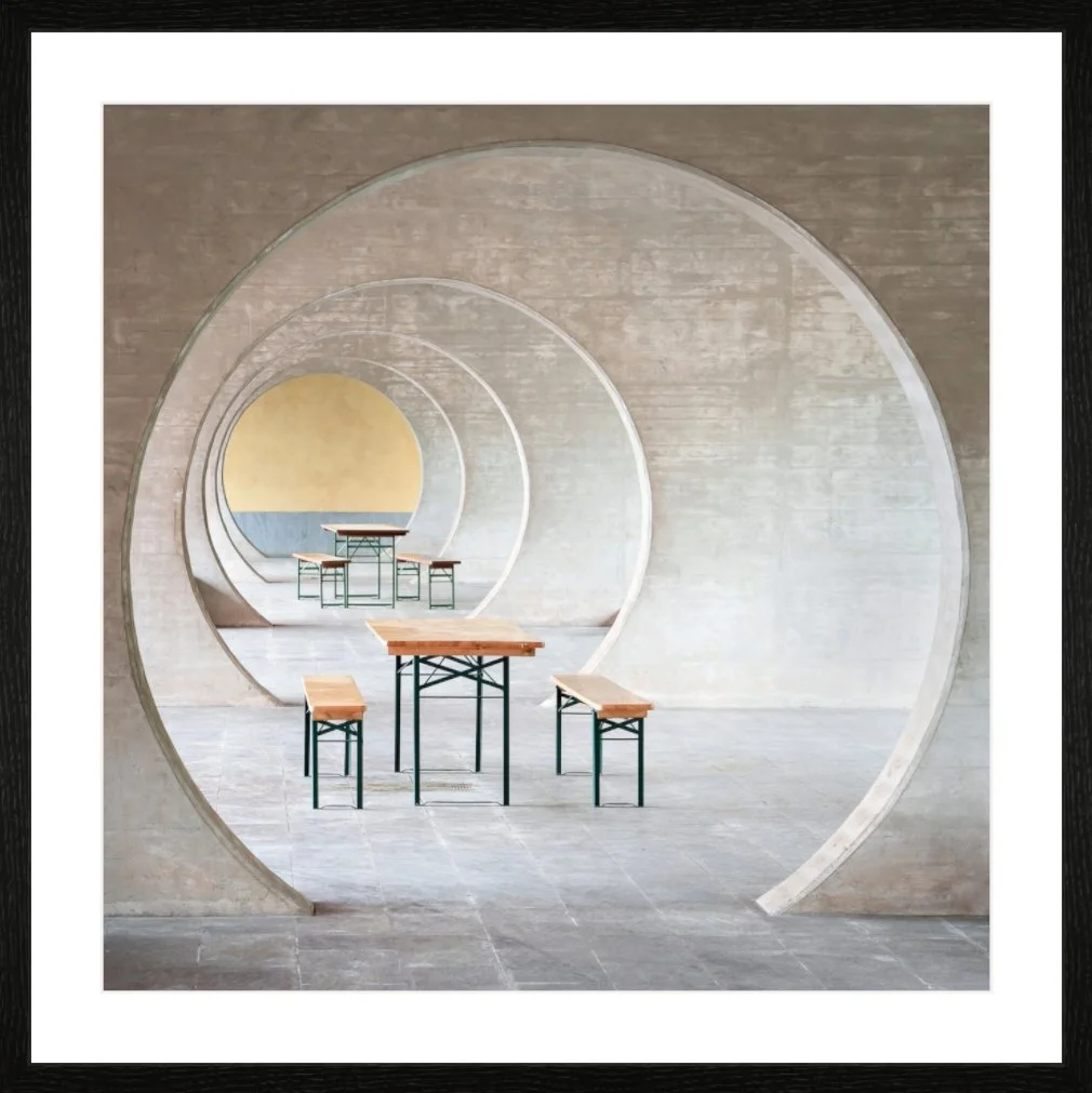 Innenaufnahme eines modernen, minimalistischen Raumes mit runden Durchgängen, Holztischen und Stühlen, helles Licht, neutrale Farben.