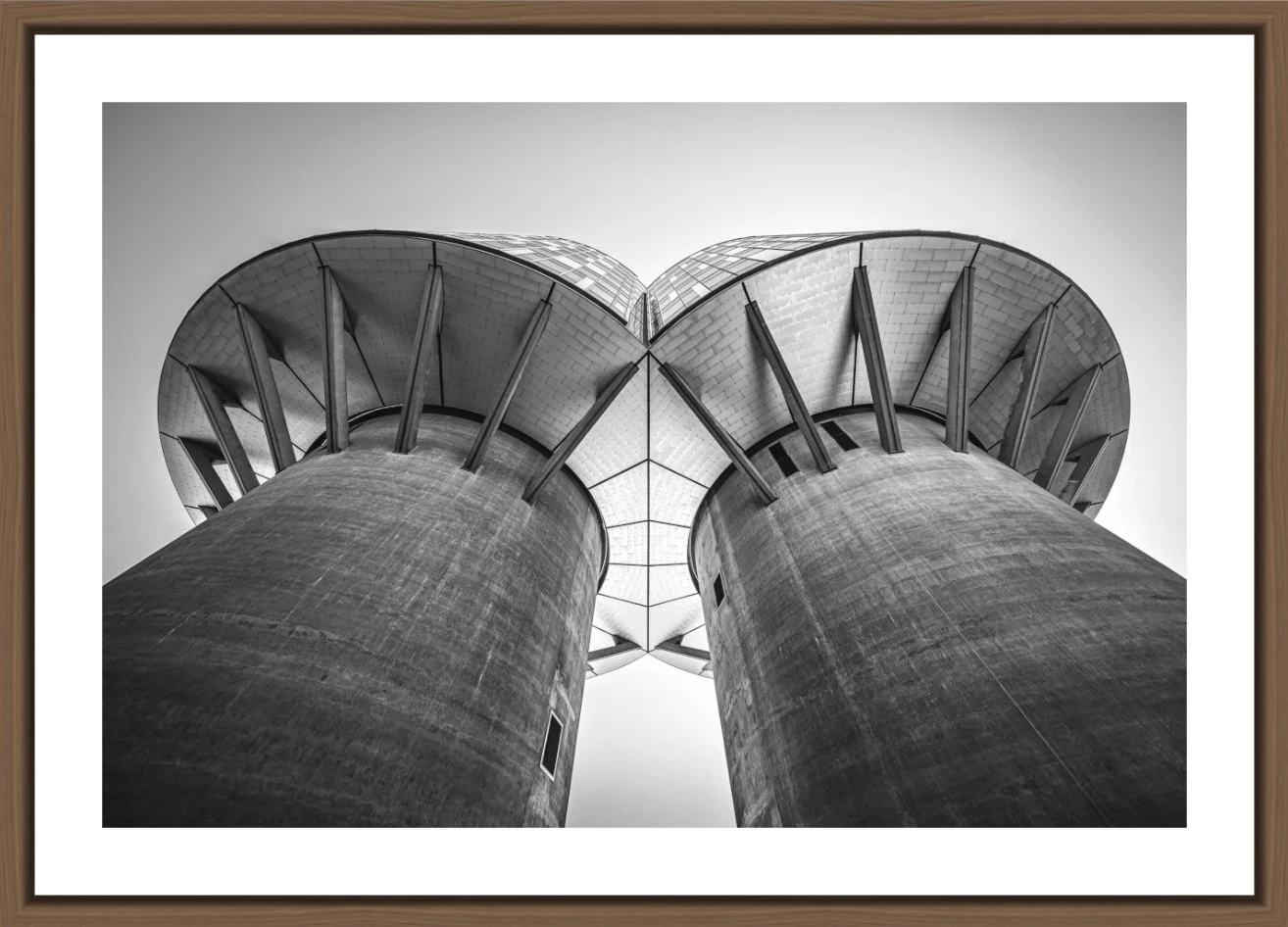 Schwarz-Weiß-Fotografie eines modernen Gebäudes mit zwei großen Betonpfeilern, die nach oben ragen, und einem gekrümmten Dach aus Glas und Metall, fotografiert aus einer tiefen Perspektive.