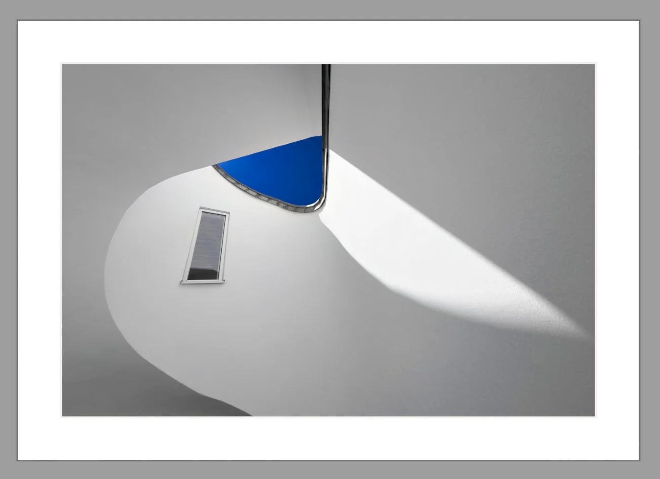 Innenaufnahme eines modernen Gebäudes mit weißem spiralförmigem Geländer, eines Fensters und blauer Himmel im Blickfeld.