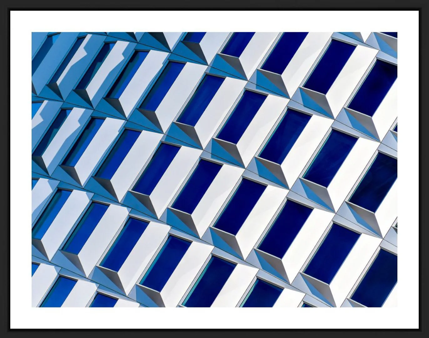 Nahaufnahme der Fassade eines modernen Gebäudes mit geometrischem Muster aus weißen und blauen Glasscheiben, die in einander übergehend sind.