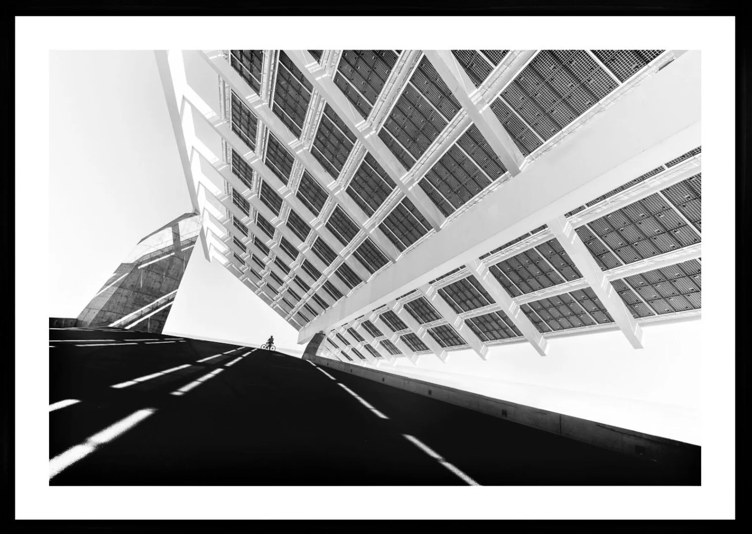 Schwarze und weiße Aufnahme eines modernen Gebäudes mit Solarzellen und Schatten auf der Straße, mit einer Radfahrerin auf der Straße