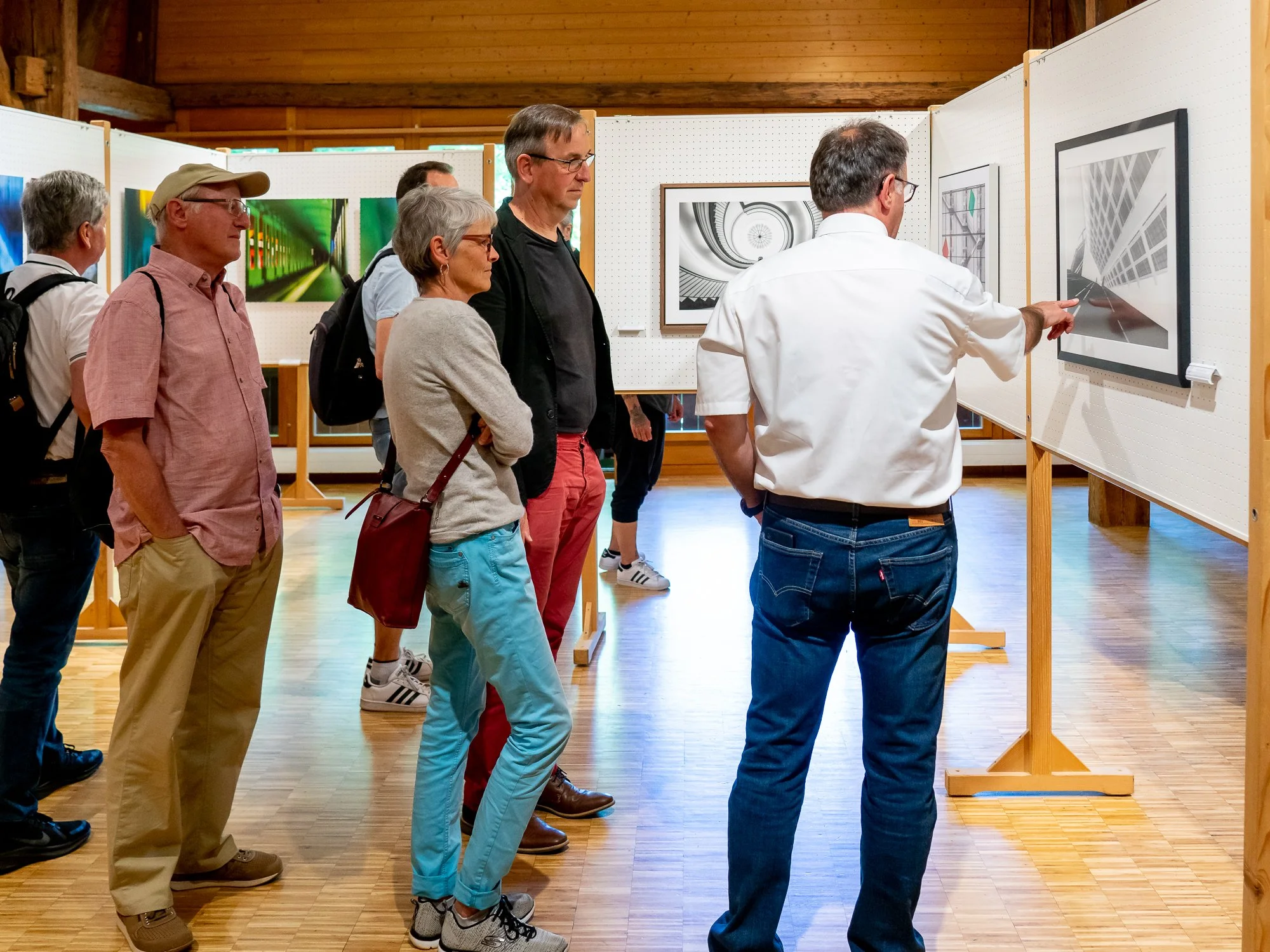 Menschen betrachten Kunstwerke in einer Galerie, wobei ein Künstler eine Skizze an einer Wand zeigt.