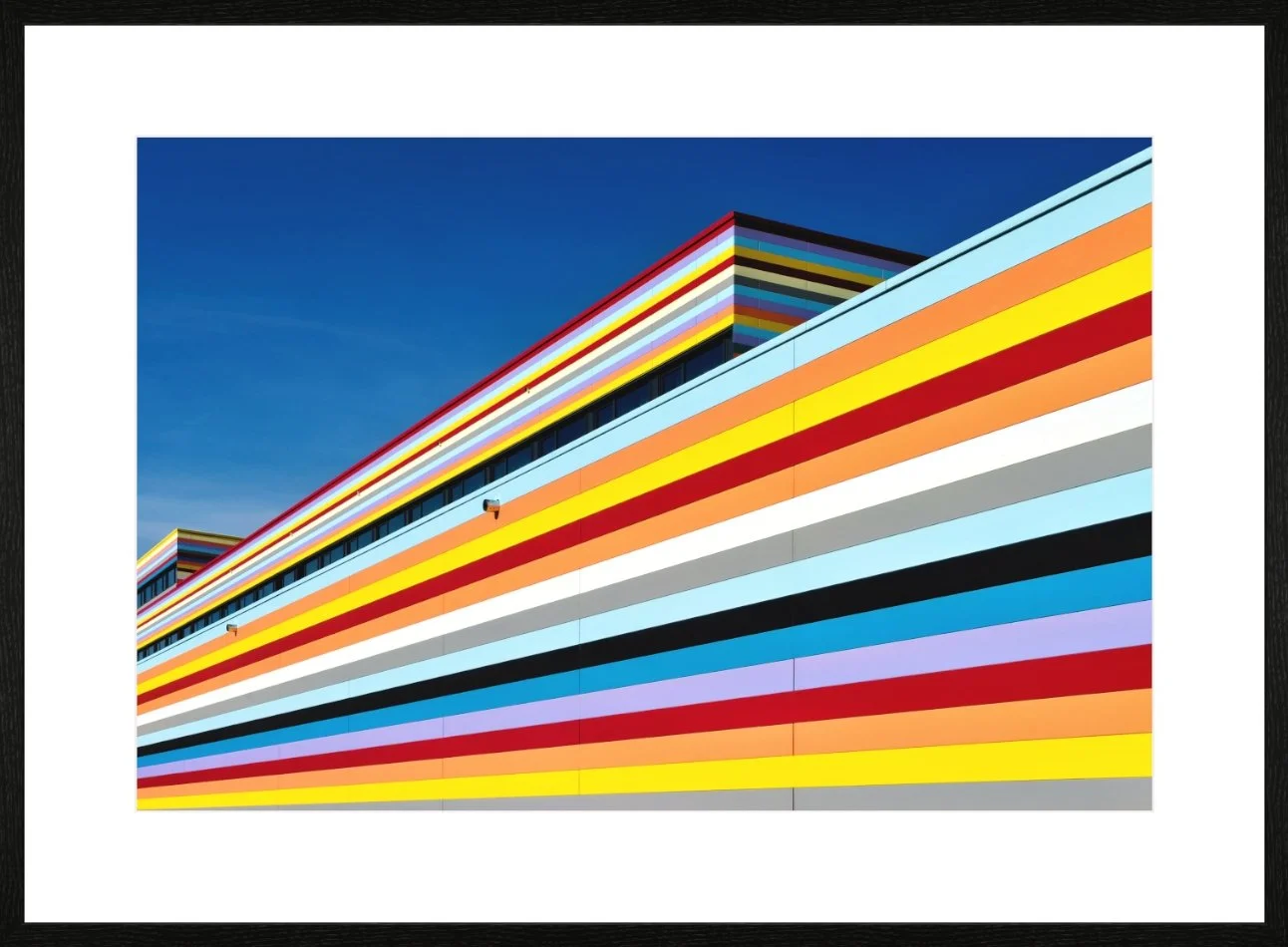 Farbenfrohes modernes Gebäude mit bunten horizontalen Streifen gegen blauen Himmel.