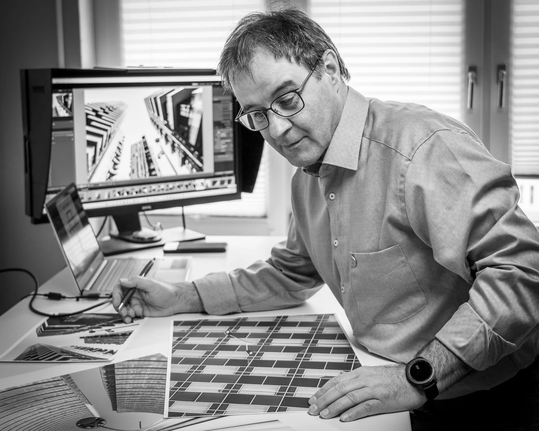 Mann arbeitet an Farbmustern in einem Büro mit Computern und Architekturfotos.