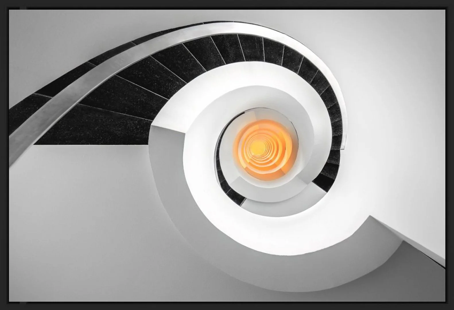 Innerer Blick auf eine spiralförmige Treppe, die nach unten führt, mit schwarzem Geländer und orange beleuchtetem Zentrum.