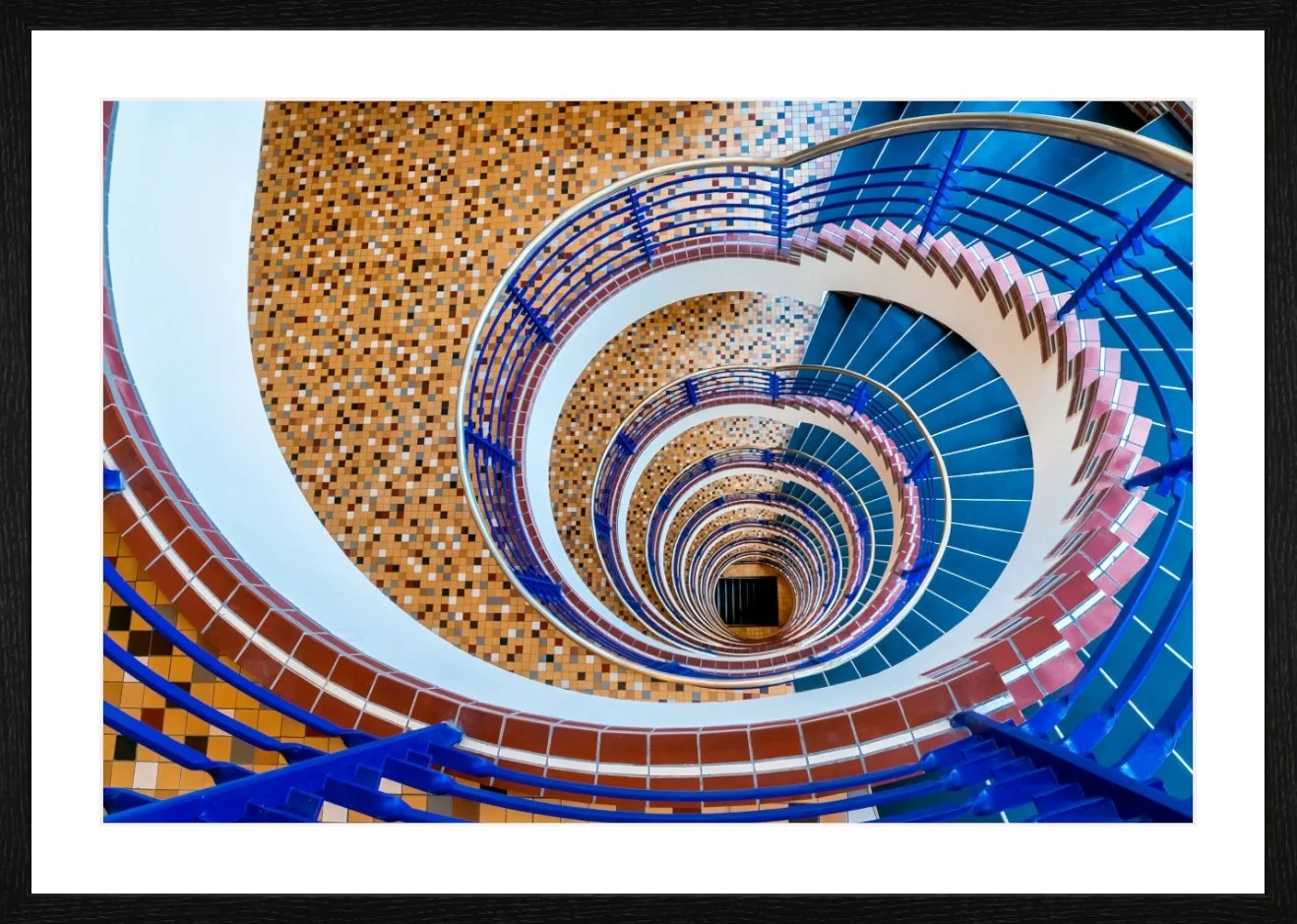 Aufnahme eines spiralförmigen Treppengeländers, das nach unten blickt, mit blauen Handläufen und einer gestreiften Bodenmuster in orange und brauntönen.