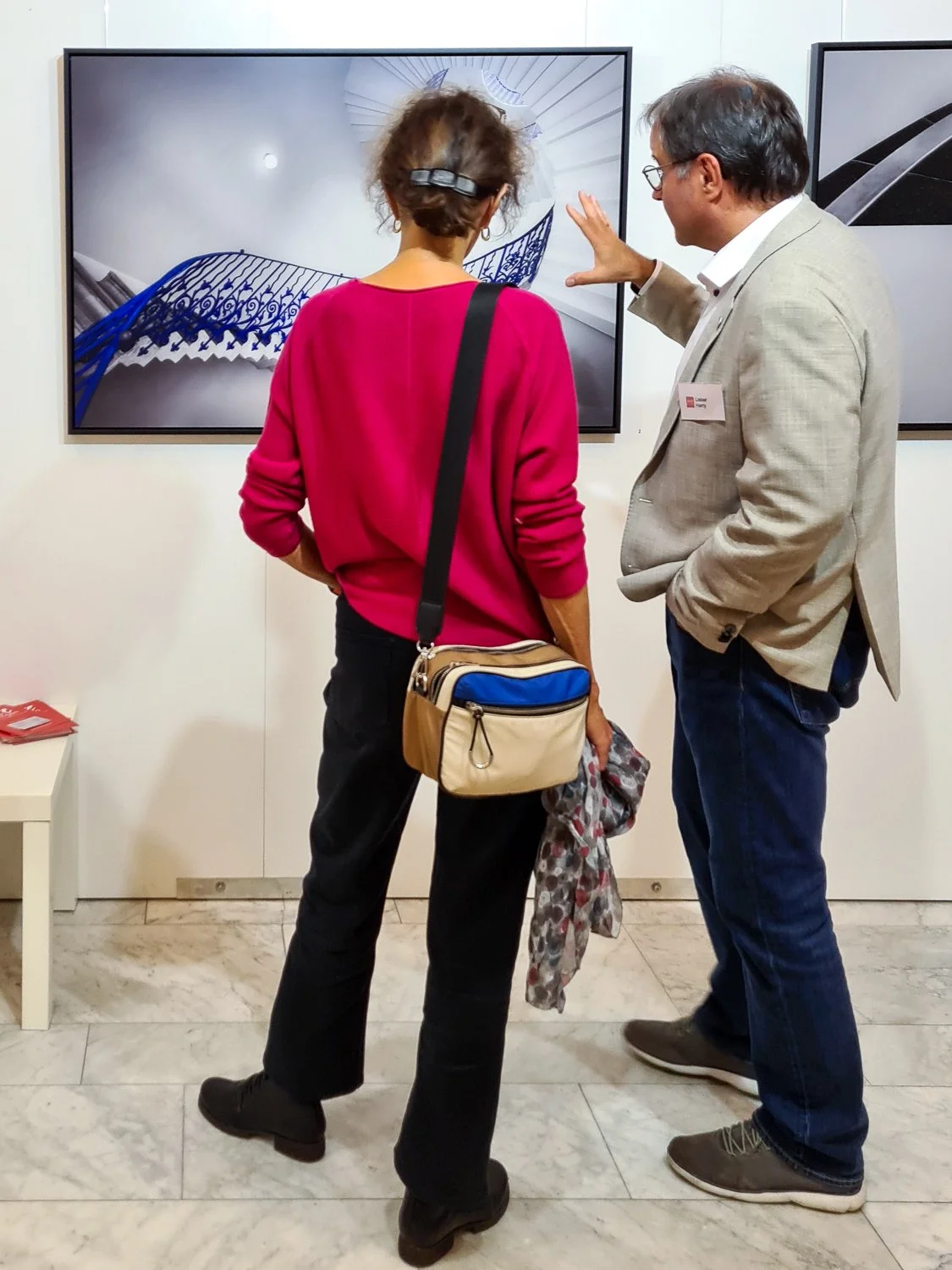 Zwei Personen, ein Mann und eine Frau, stehen vor einem Bildschirm und betrachten eine Digitalaufnahme eines Gebäudes mit blauen Geländern.