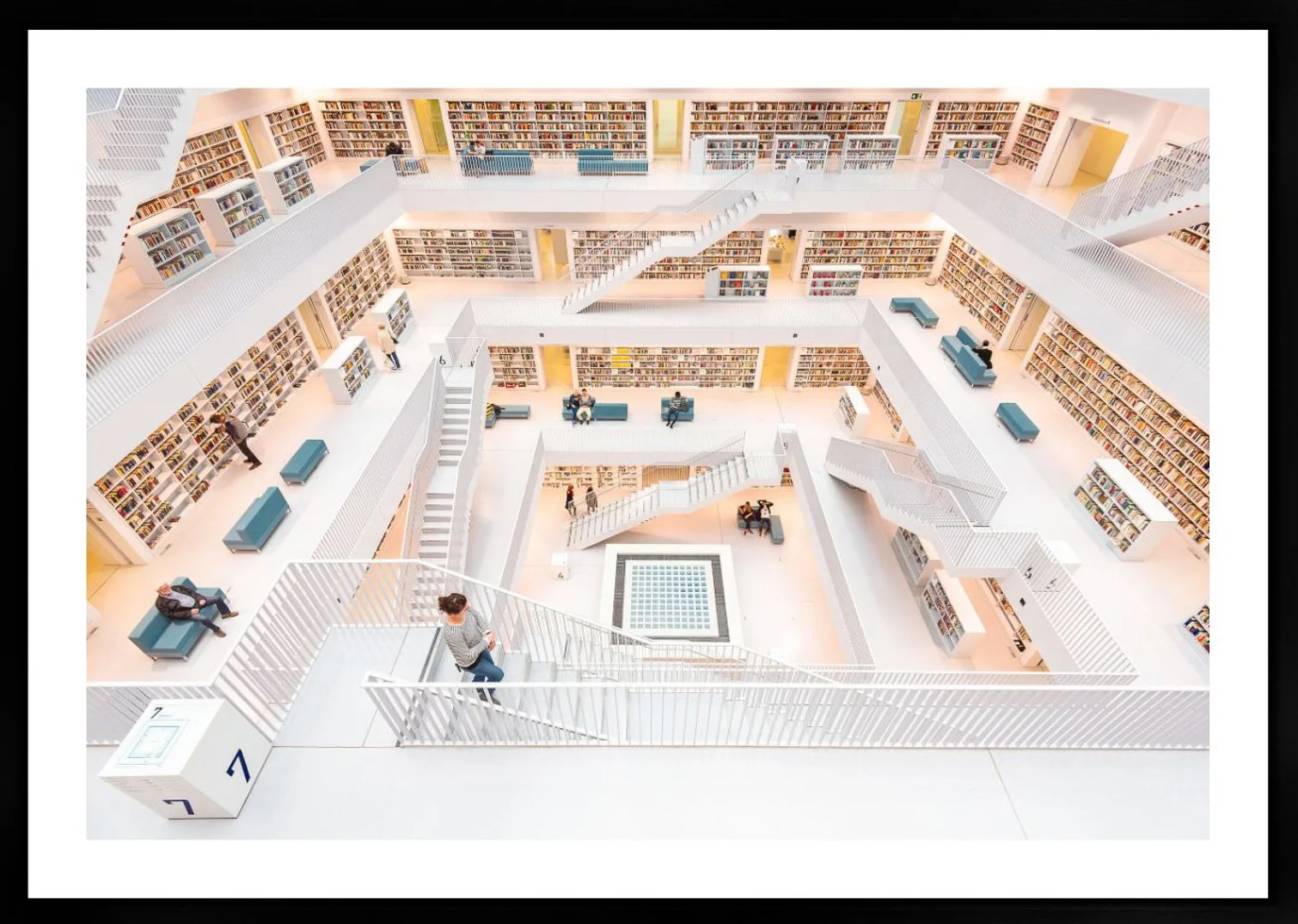 Innenansicht eines modernen Mehrgeschossigen Bücherhauses mit weißen Regalen, Lesebereichen und Menschen, die lesen oder durch die Regale gehen.