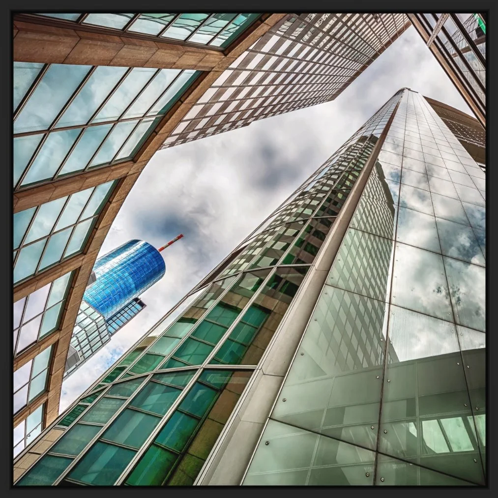 Aufnahme von mehreren hohen modernen Glas- und Stahlgebäuden, Blick nach oben, mit Wolken am Himmel im Hintergrund.