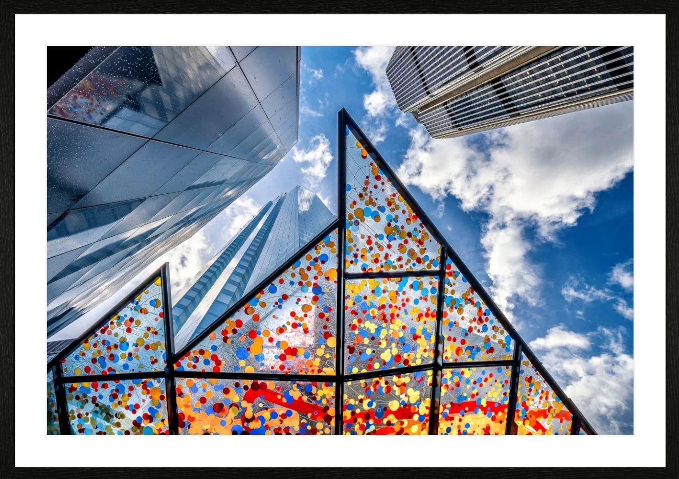 Himmel mit Wolken über modernen Wolkenkratzern und einer bunten, verspiegelten Glasfassade