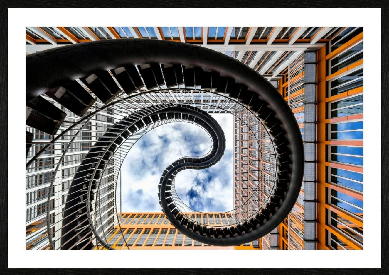 Innenaufnahme eines spiralförmigen Treppens in einem modernen Gebäude mit Blick nach oben auf den Himmel.