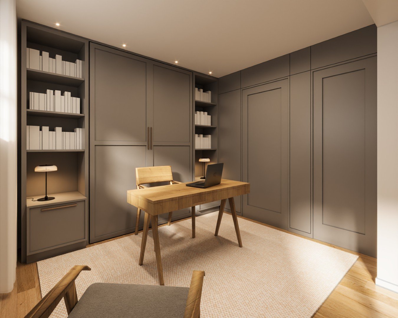 A minimalist home office with dark gray built-in cabinets, open bookshelves filled with white books, a wooden desk with a laptop, a matching wooden chair, a small side table with a lamp, and a beige rug on hardwood flooring.