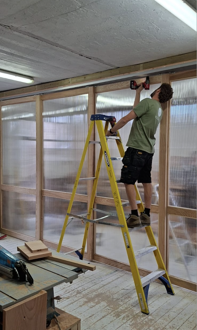 Man fitting doors to sliding rail on a ladder
