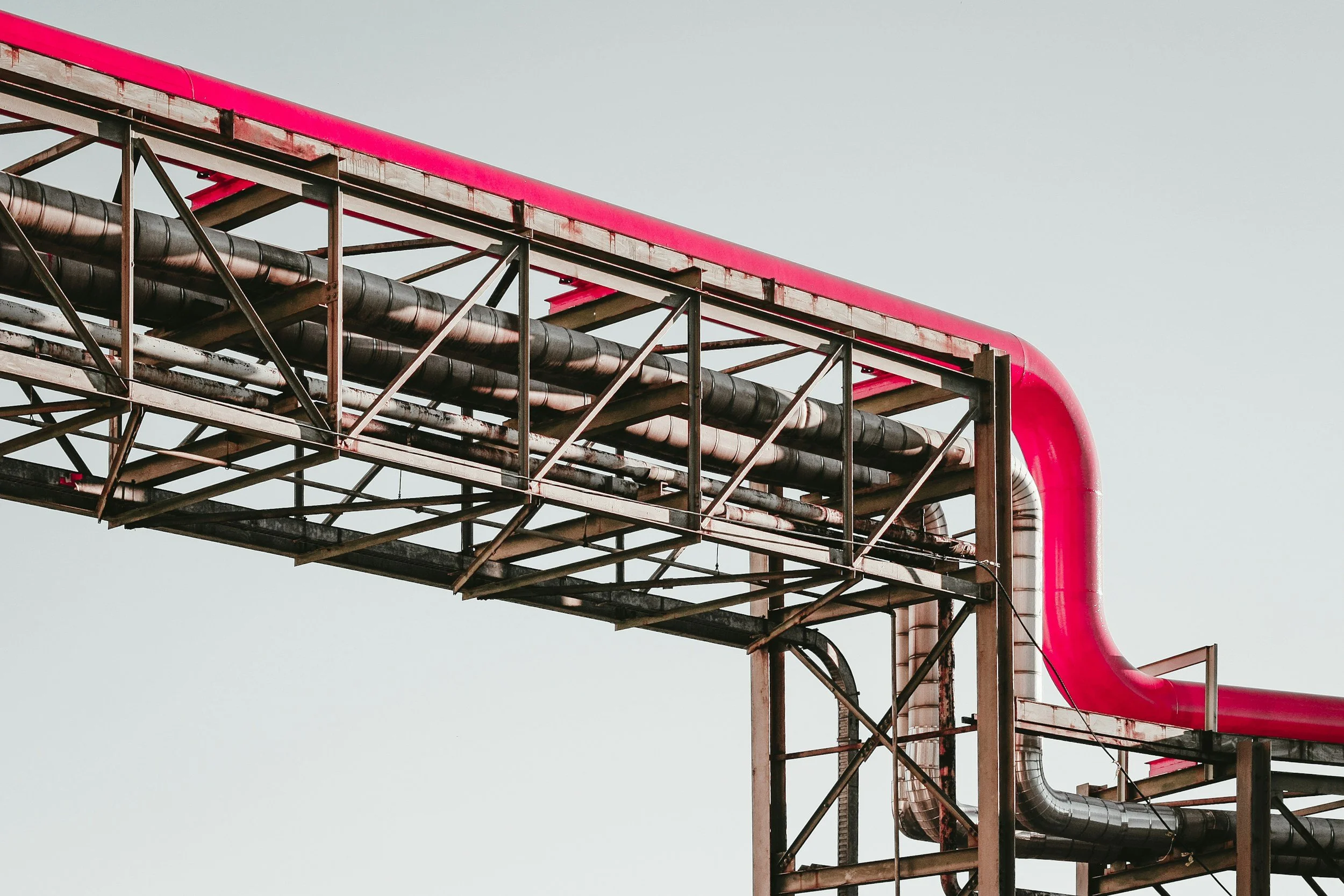 Industrial infrastructure with pipes and metal framework, including a pink pipe, against a clear sky.