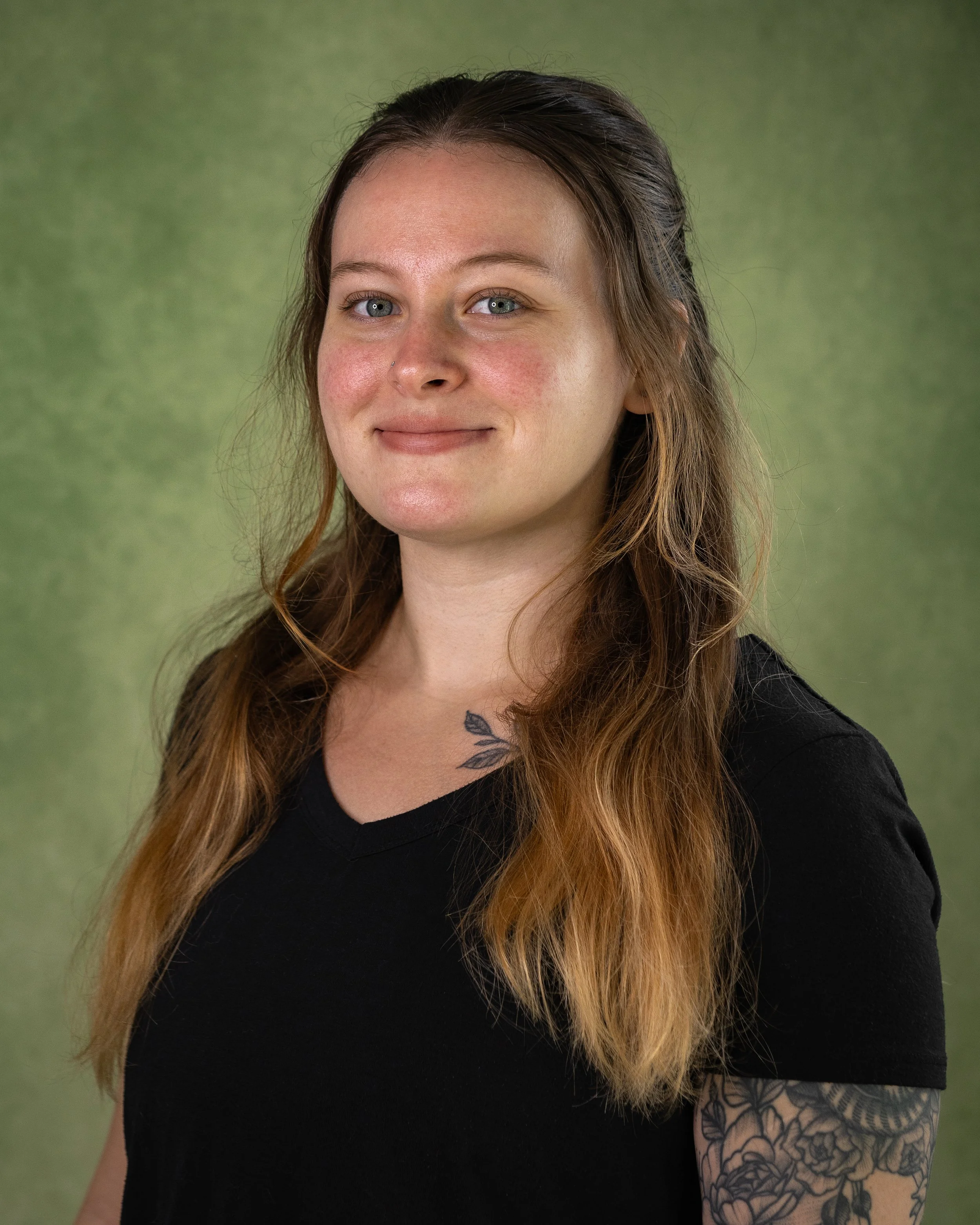 A young woman with long, wavy hair, wearing a black shirt, standing against a green background.