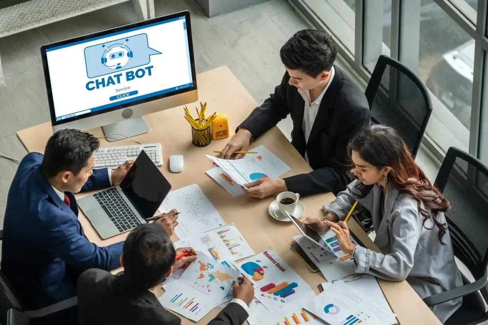 Team of professionals meeting in an office with charts and a computer screen showing a chatbot interface, symbolizing the rise of AI tools in legal and business discussions.