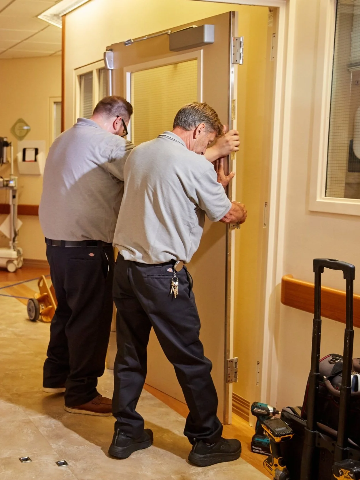 Two men installing a fire  door in a California hospital, with tools and equipment nearby.