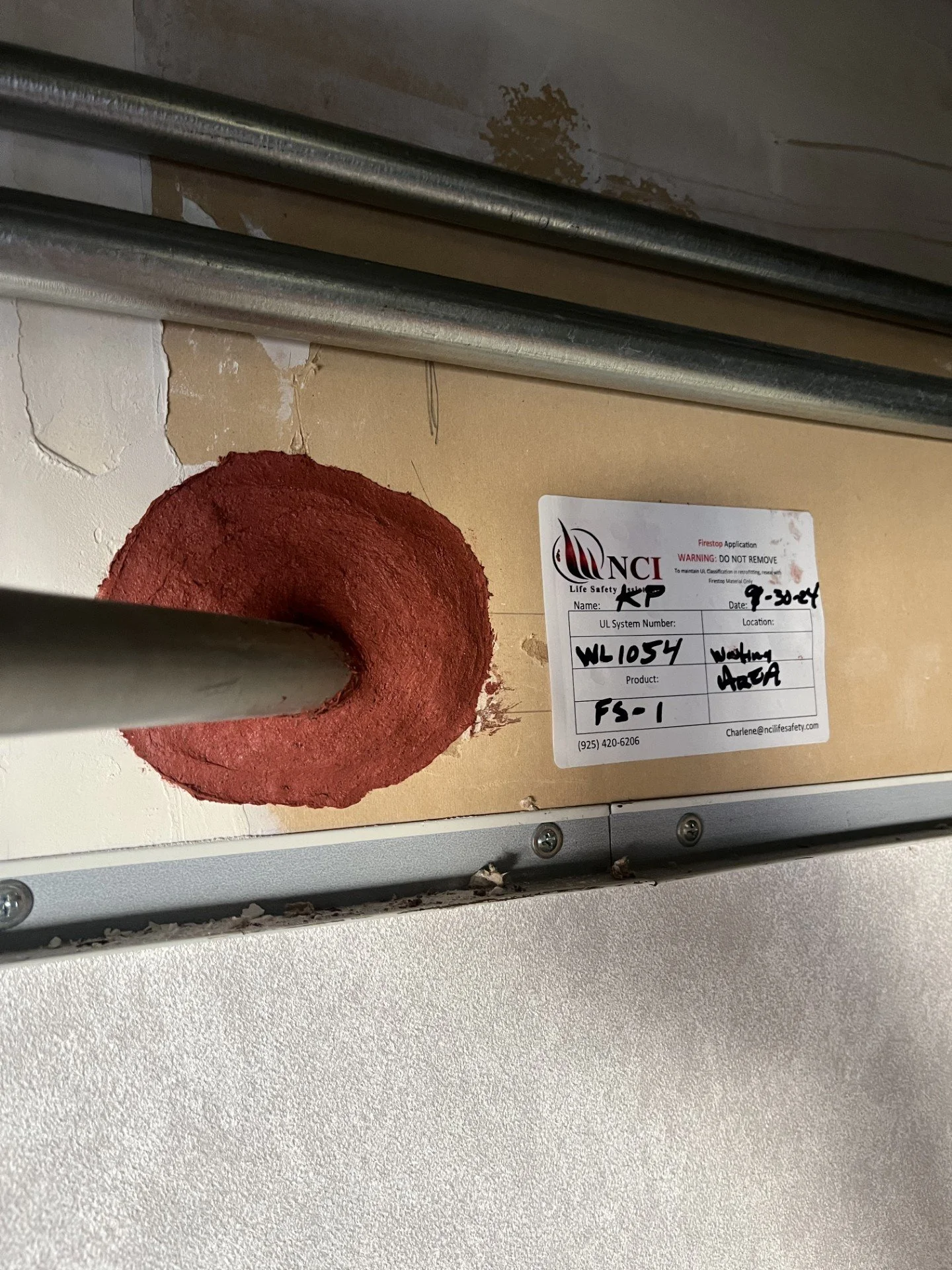Close-up of fire sprinkler pipe penetrating the ceiling with a red seal around it, and a label indicating fire suppression system information.