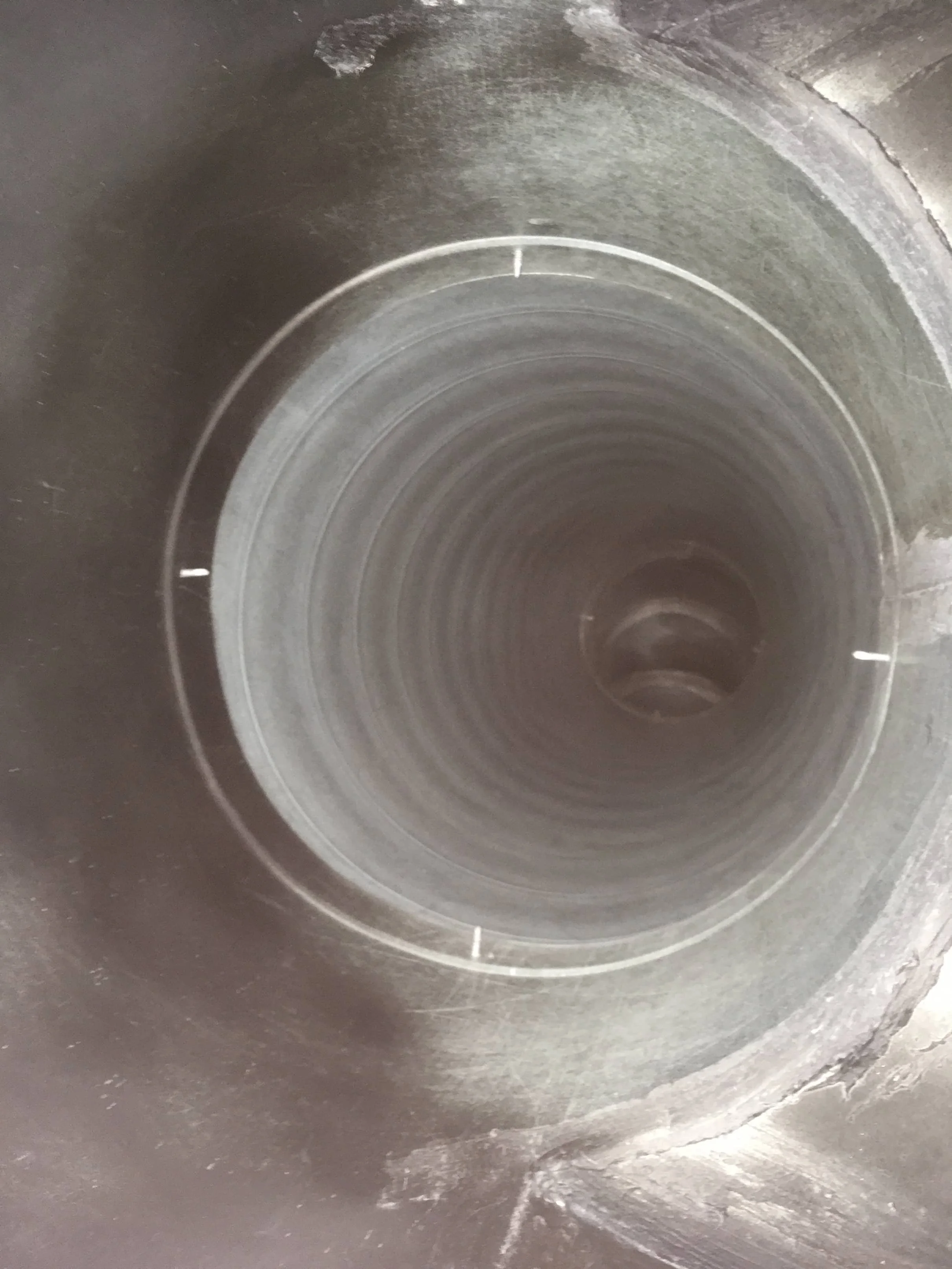 Looking into a metal pipe or tube, showing its circular, concentric interior with slight reflections and shadows.