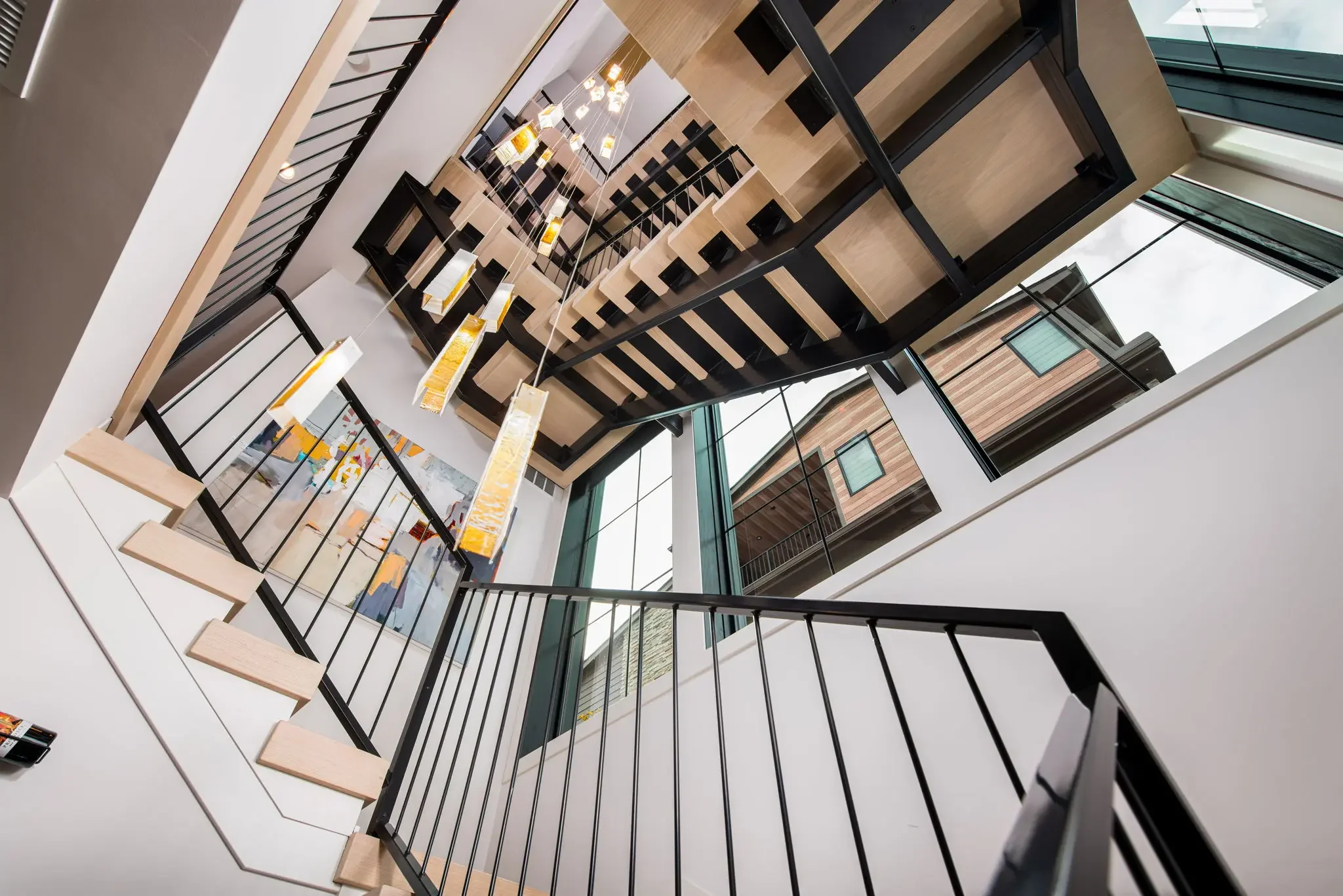 Lower angle up a modern wood and metal staircase with floating light fixture