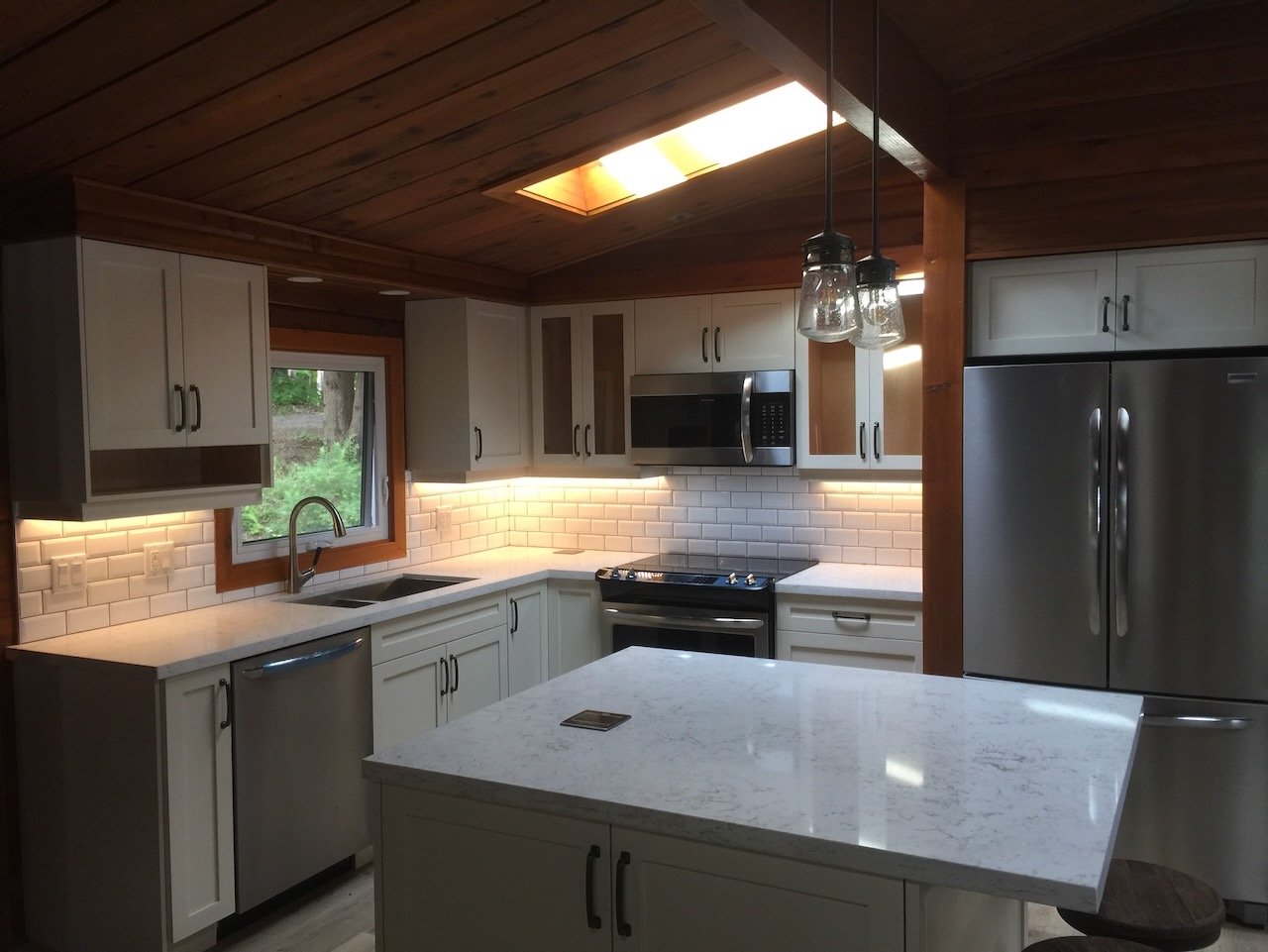 Modern kitchen with white cabinetry, stainless steel appliances, and a marble countertop island. Features subway tile backsplash and pendant lights.