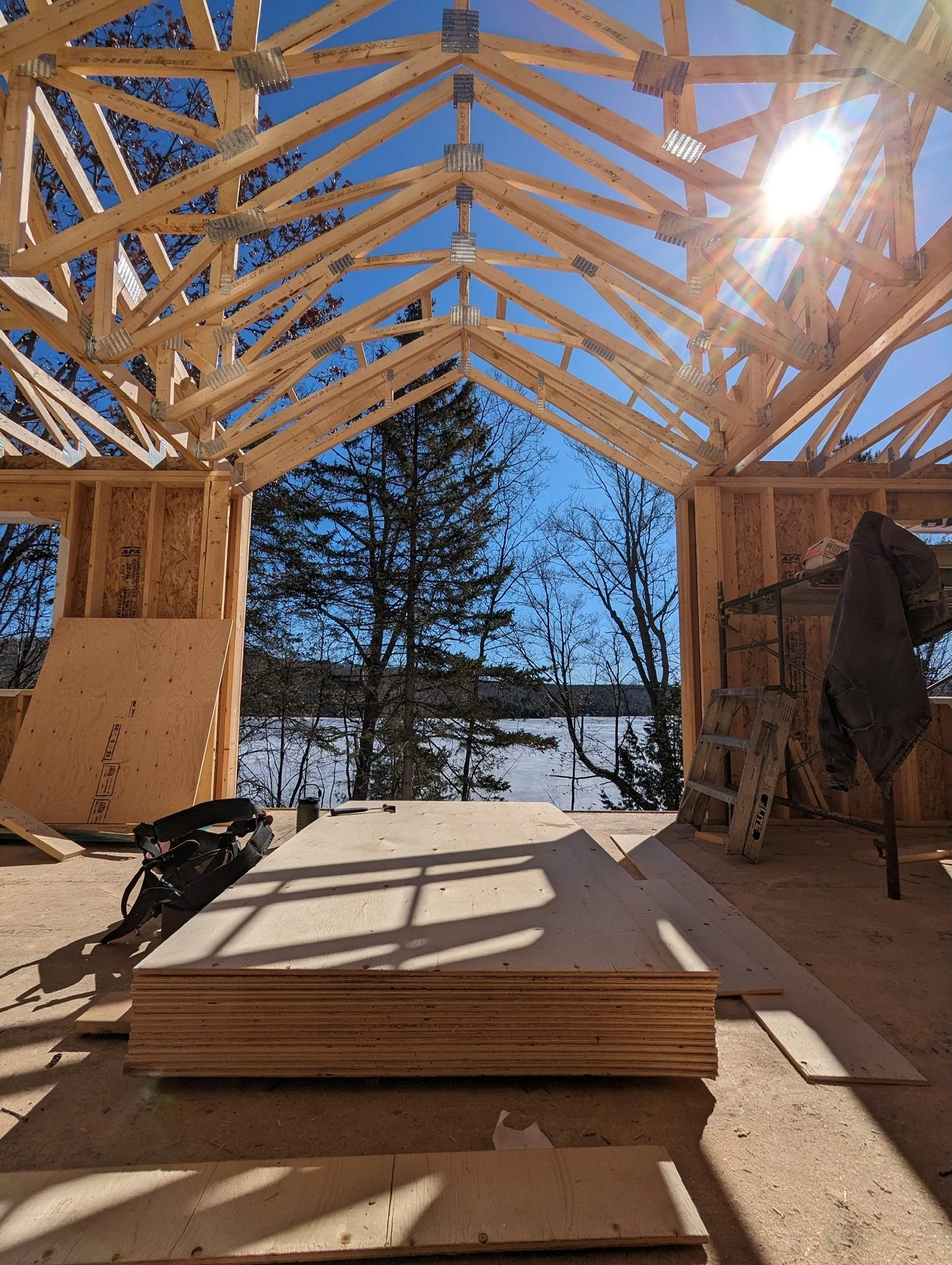 Construction site with wooden trusses, plywood stack, and a ladder under blue sky