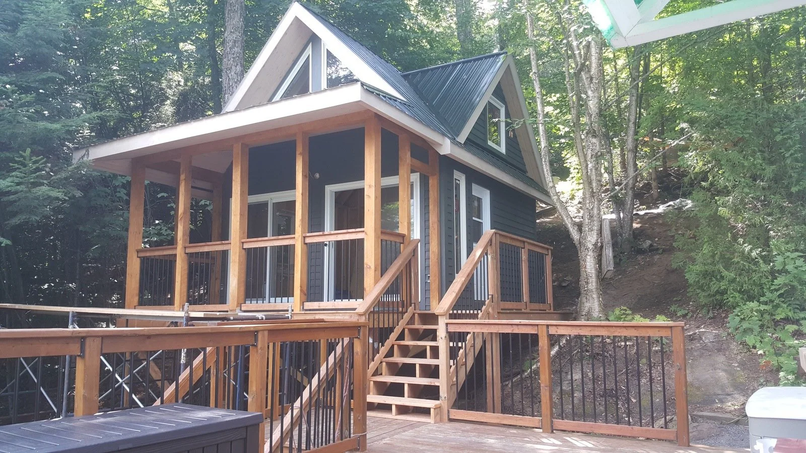 A-frame cabin with wood and metal railing on a deck, surrounded by trees.