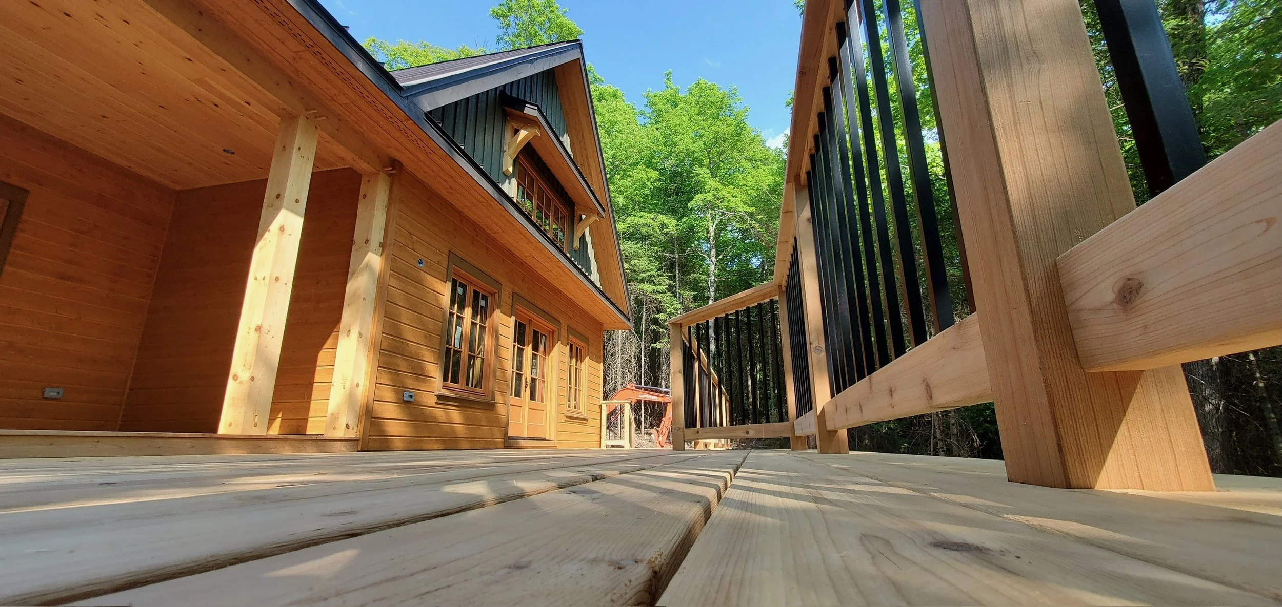 Wooden cabin with porch and railing, surrounded by trees and clear blue sky.