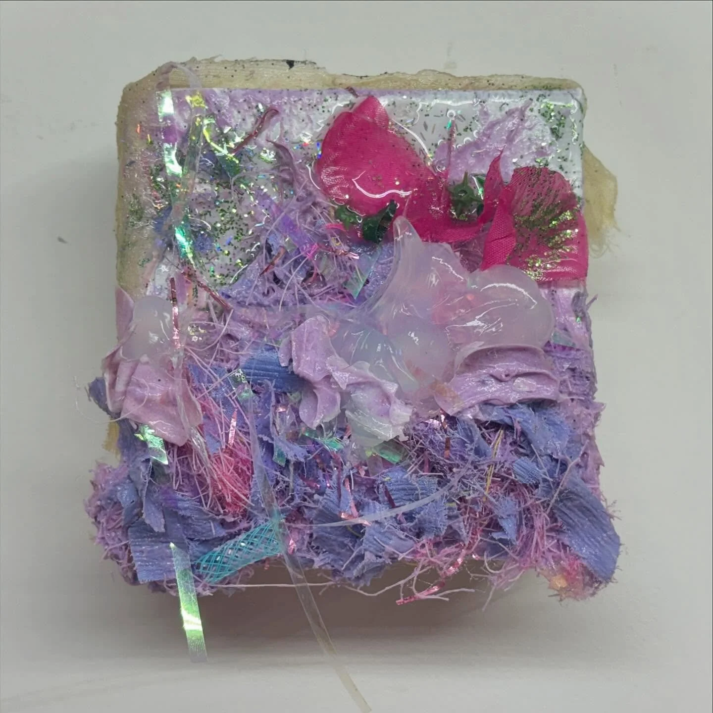 untitled (c) 
4x4x2.5in
caulk, resin, glitter, artificial flowers, cellophane, hair, sourced fabric, and deco mesh on canvas 
2024