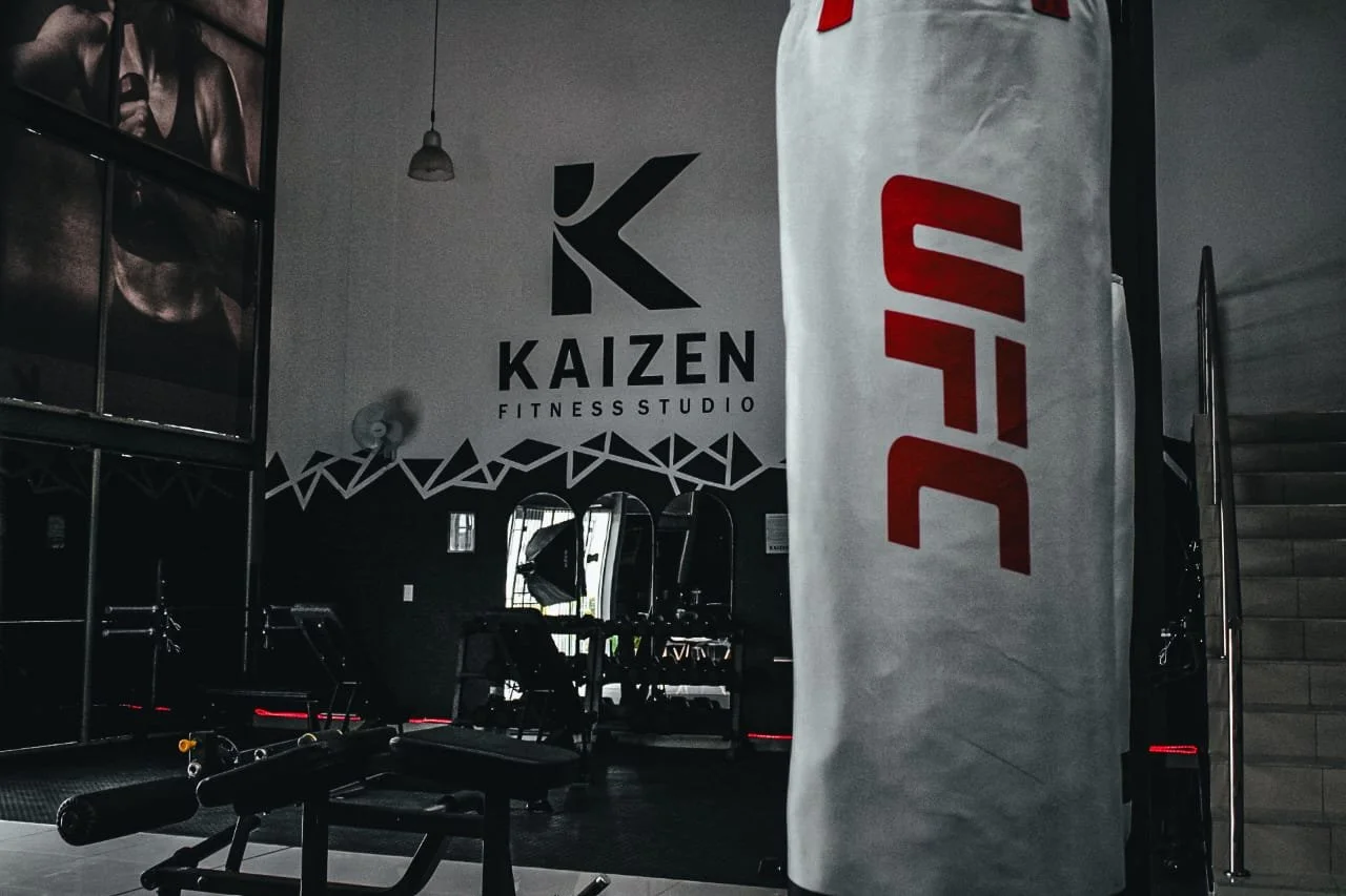 Interior of a fitness studio with workout equipment, mirrors, and a prominent UFC banner.