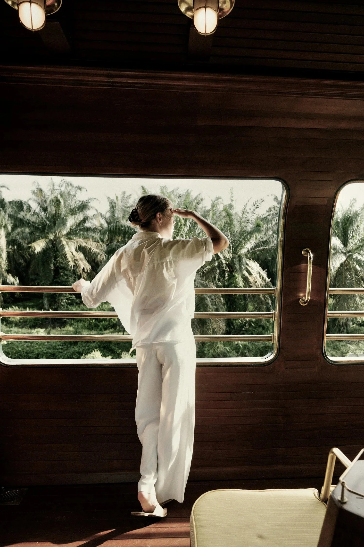 Woman in white looking out the window of a luxury train past palm trees