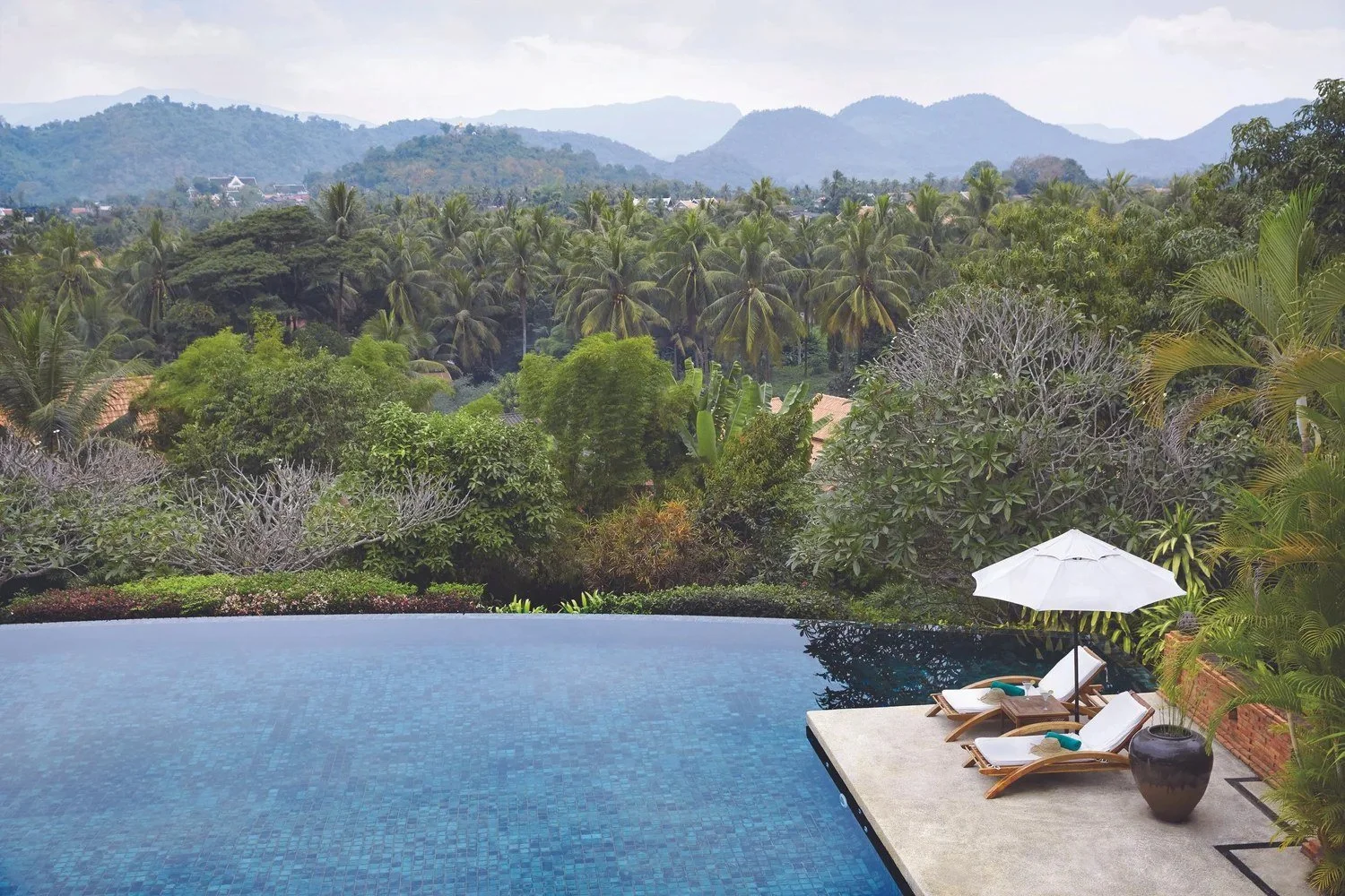 Infinity pool with umbrellas and loungers overlooking jungle and mountains at an Asian resort