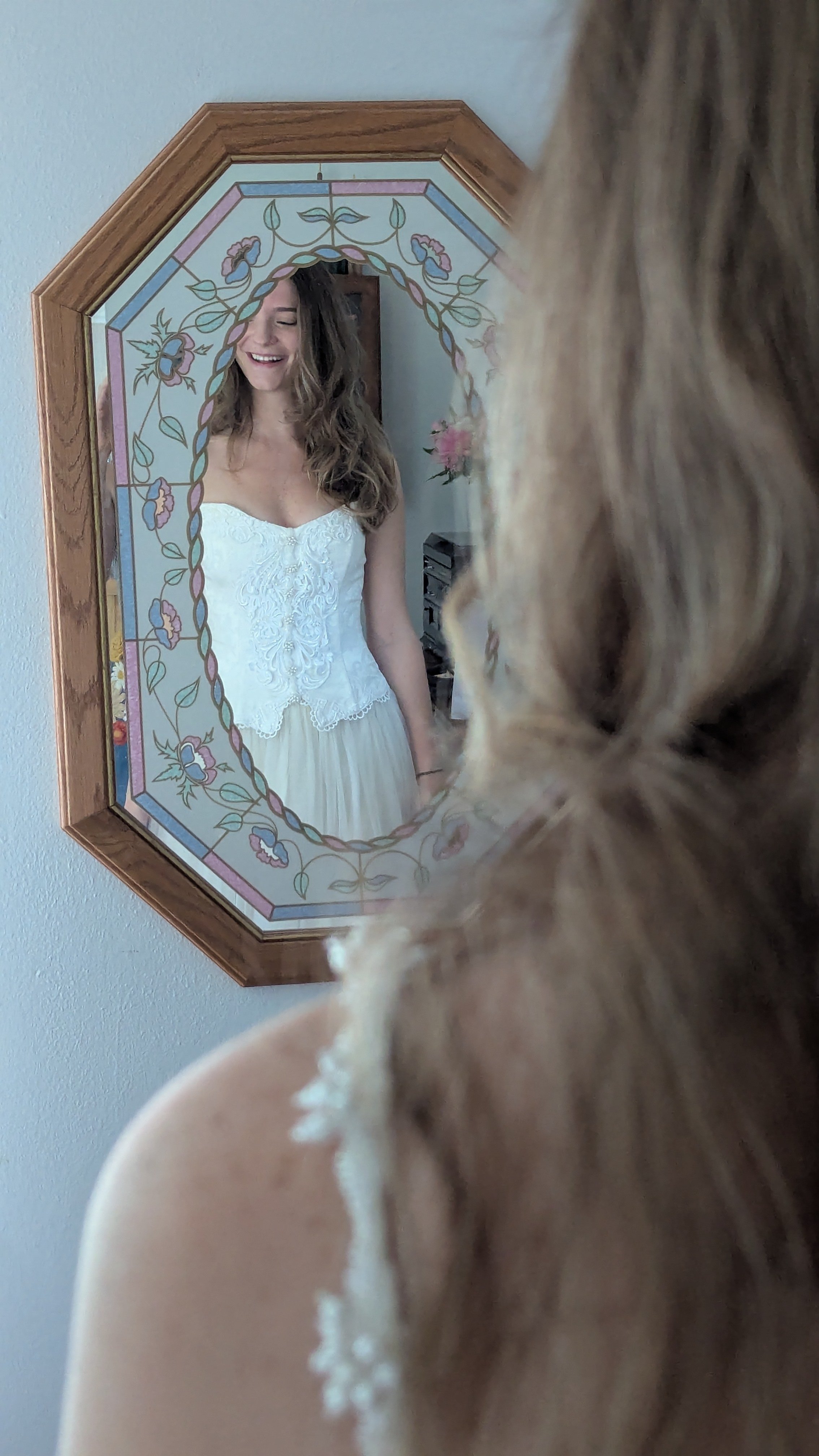 A woman in a white dress looking into a mirror, with a dog in the foreground partially obscuring the view.
