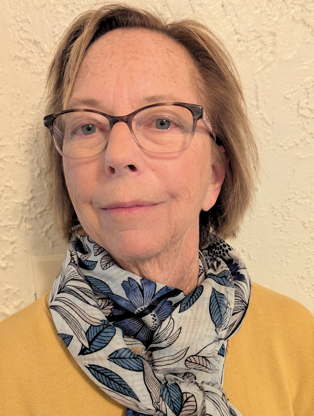 Person wearing glasses and a floral scarf against a textured wall.