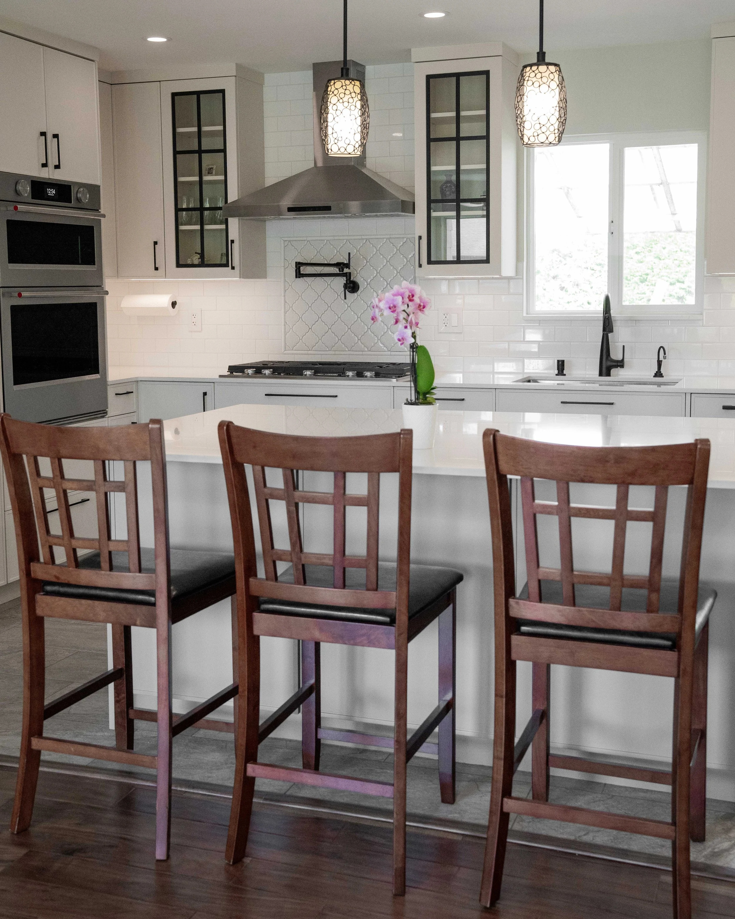 WorkPro Contracting 119 Ave Renovation: Kitchen Photograph featuring a large kitchen island, white cabinetry and black hardware, white backsplash, and bright cabinet lighting