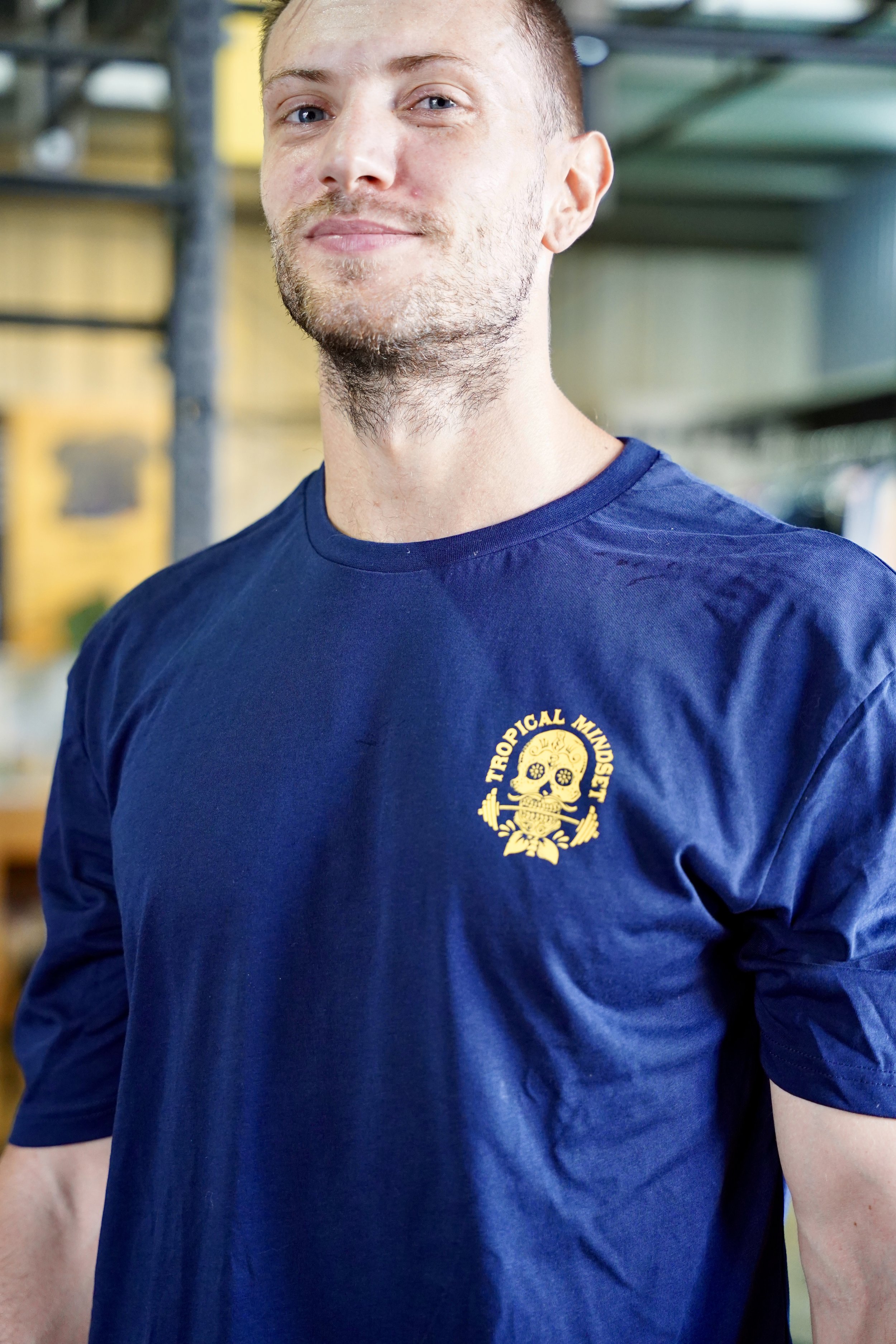 L’image montre un homme fièrement debout avec un t-shirt bleu foncé et un logo sur le cœur de tête de mort mexiquaine