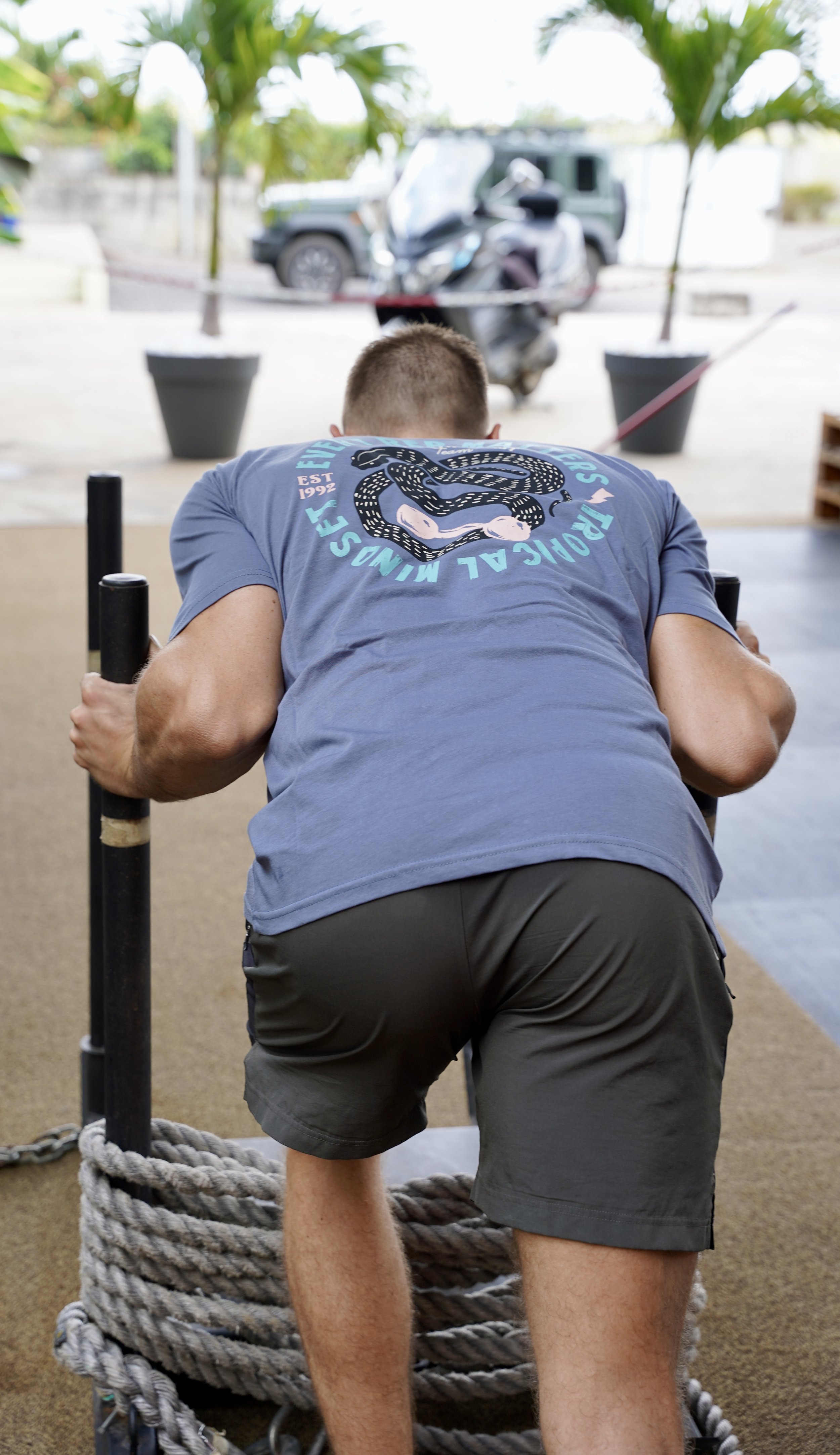 L’image montre un homme de dos poussant un traîneau et habillé d’un short et d’un t-shirt bleu