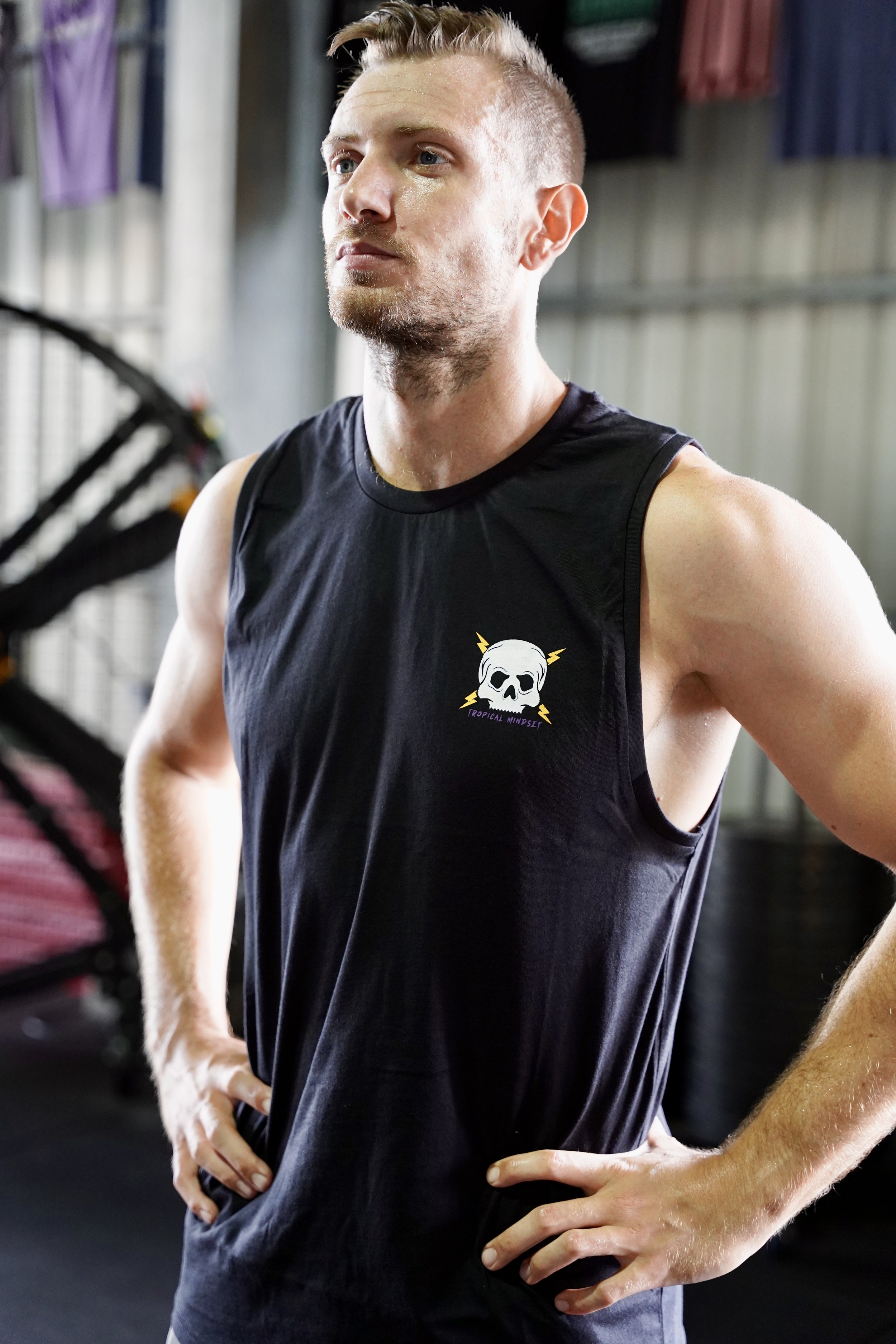 L’image montre un homme de face vêtu d’un singlet noir avec comme logo une tête de mort et des éclairs sur la poitrine